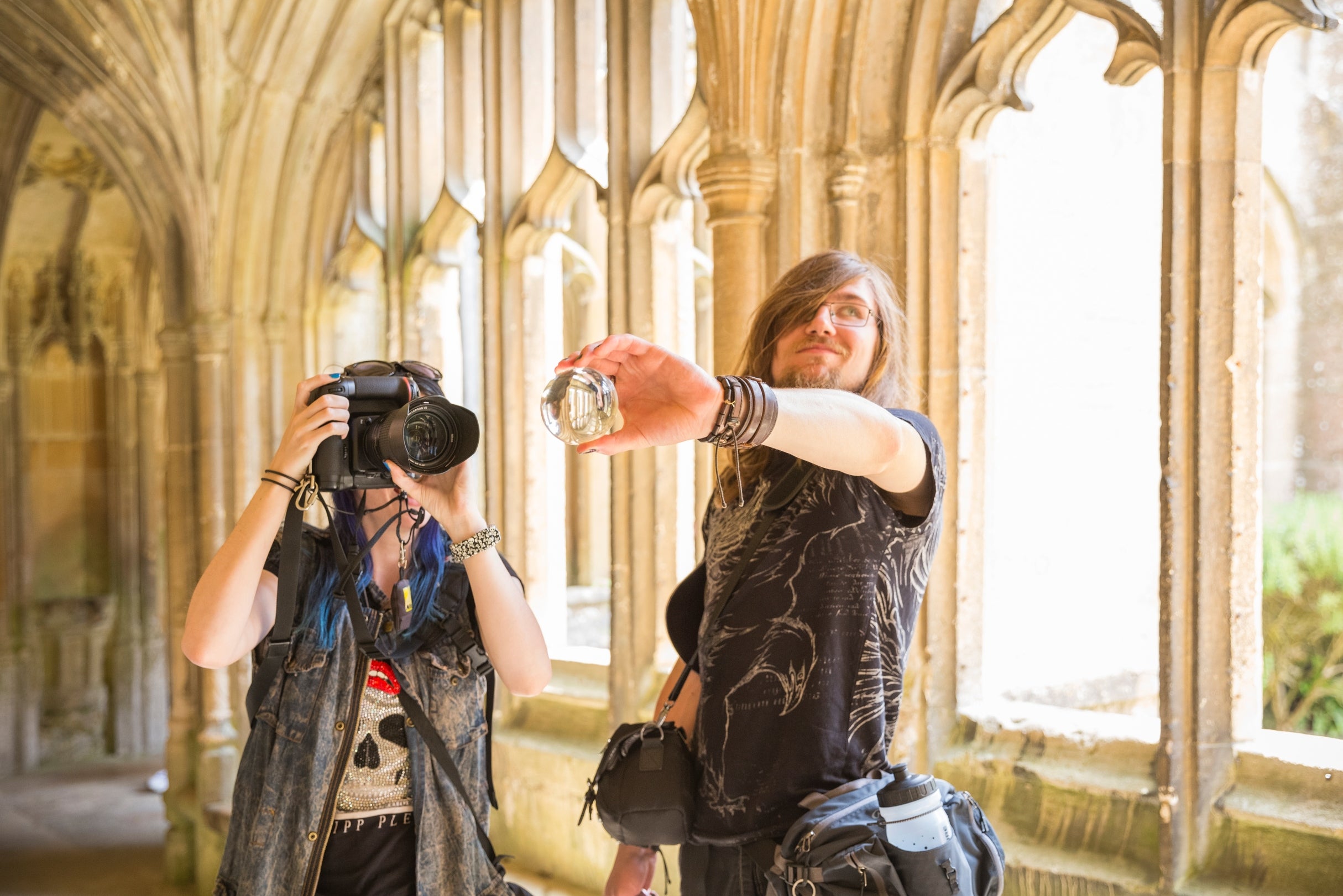 Two people take photos in the Cloister at Lacock Abbey, one uses a digital camera whilst the other holds a glass prism for the camera to view the scene through.