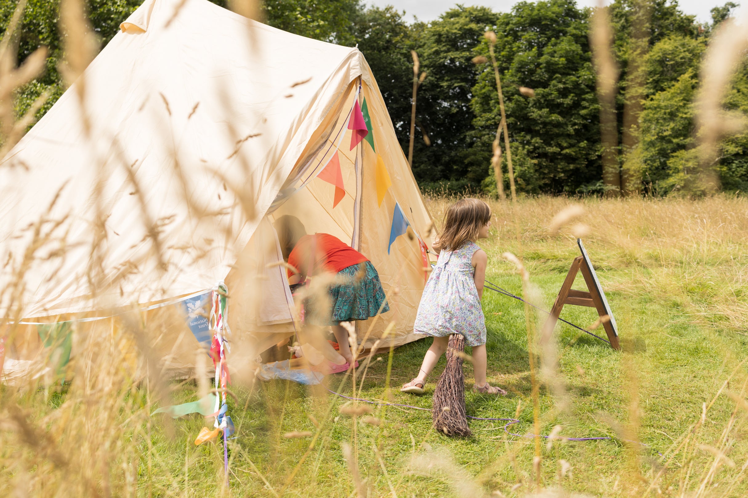 Children explore the dress up tent in the parkland during Lacock's summer of play. One child is riding a broom while the other rummages for something to dress up in.