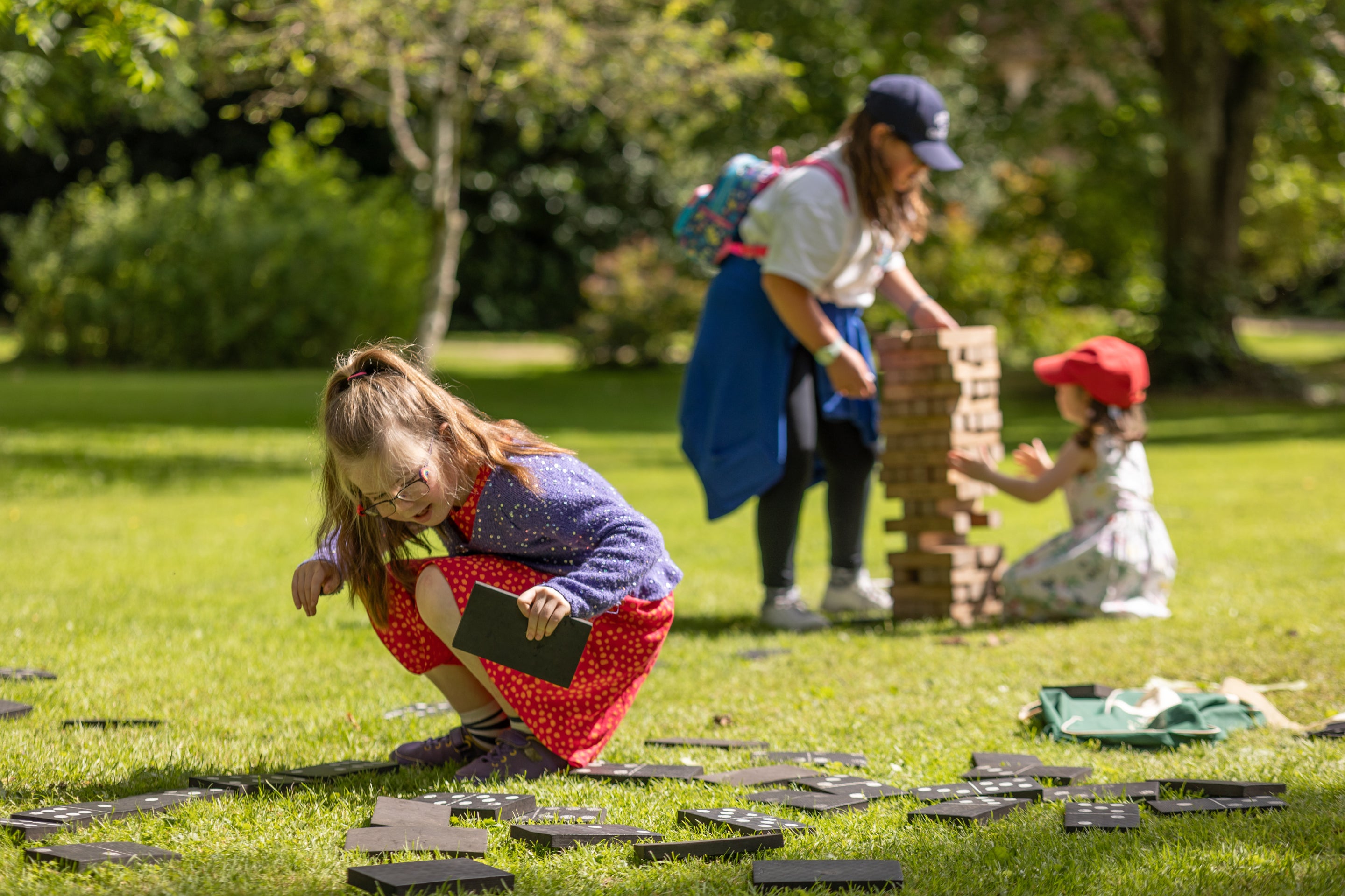 Children play with a giant dominos set on a green lawn in the sunshine.