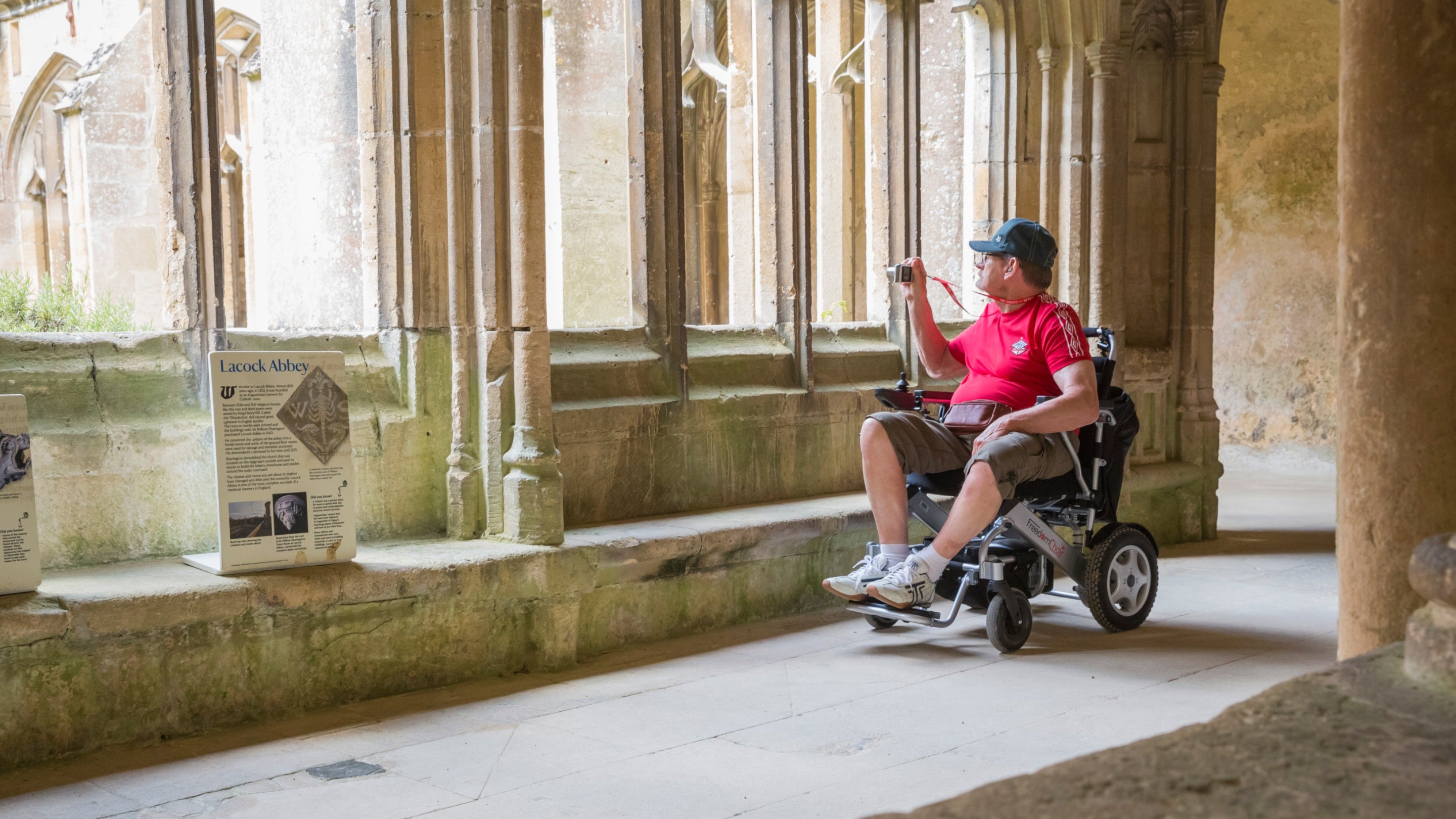 A wheelchair user taking a photograph through open stone mullions