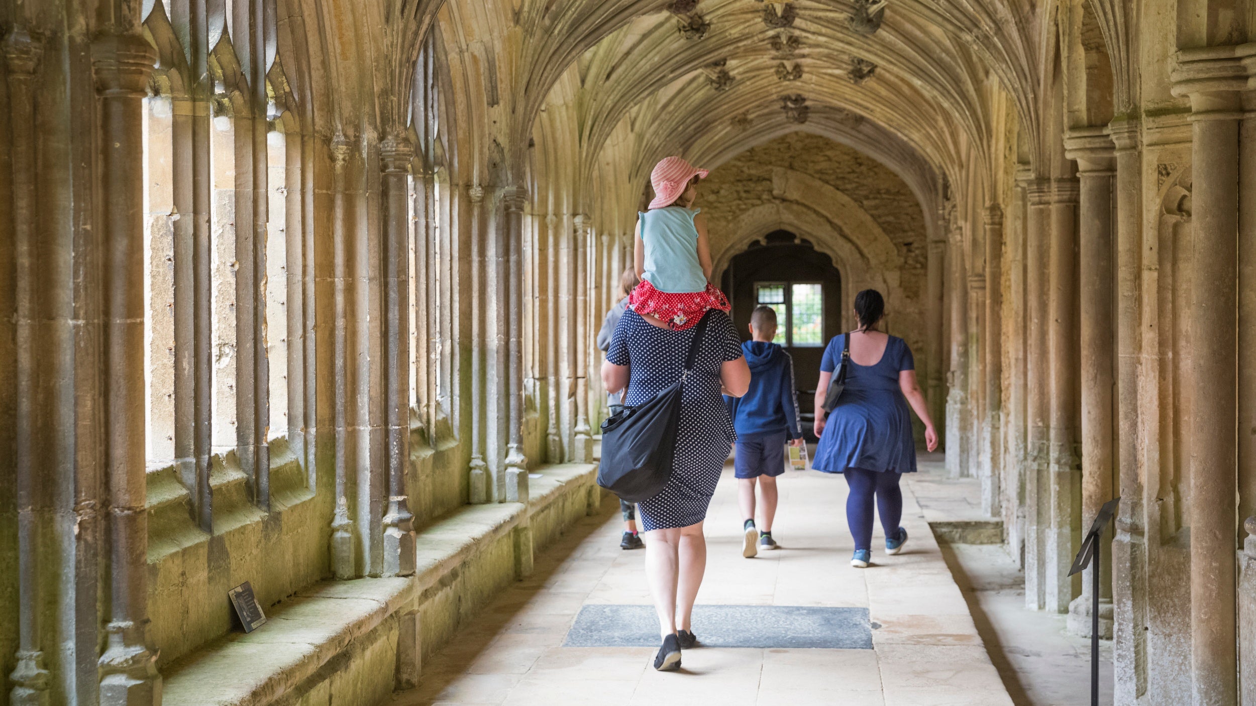 Family in summer clothes walking through the cloister at Lacock Abbey