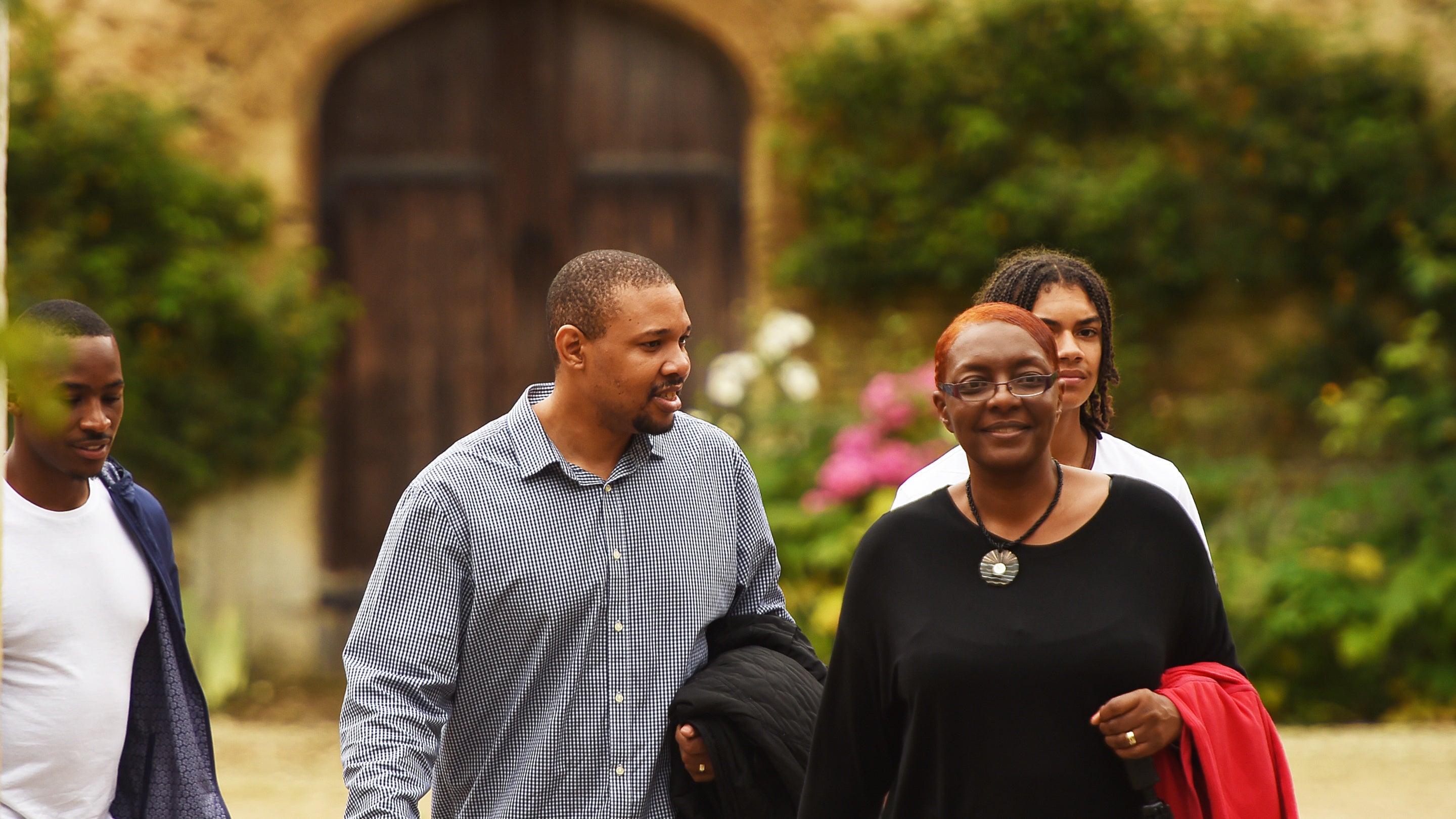 A group of four people are walking outside at Lacock, with an ornate wooden arched door set into a stone wall visible in the background.