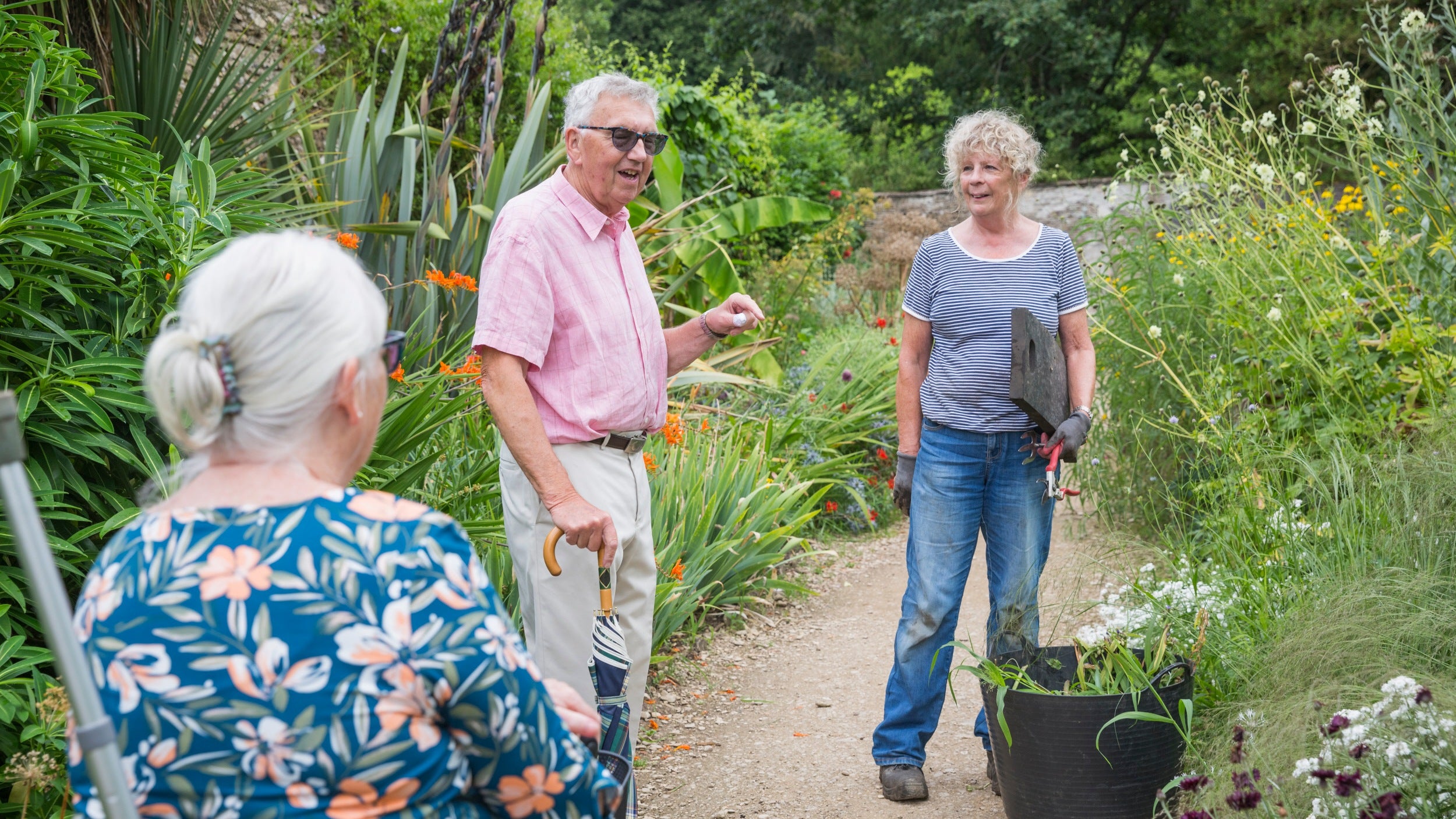 Volunteer gardener talking to visitors in the garden amidst abundant planting