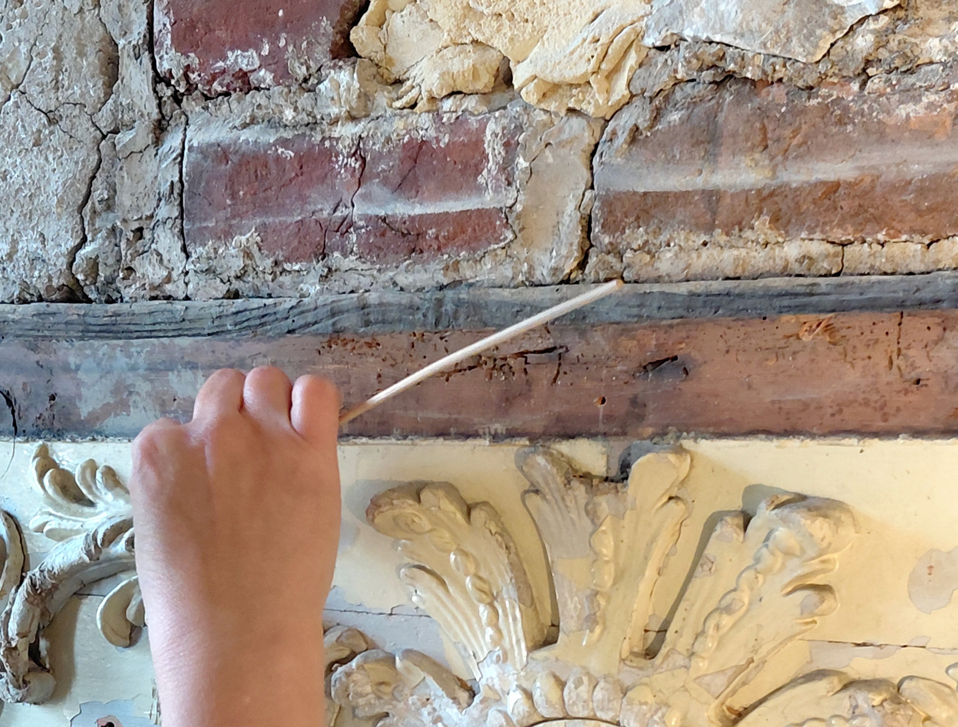 A conservator works on the papier mache detailing of a fireplace