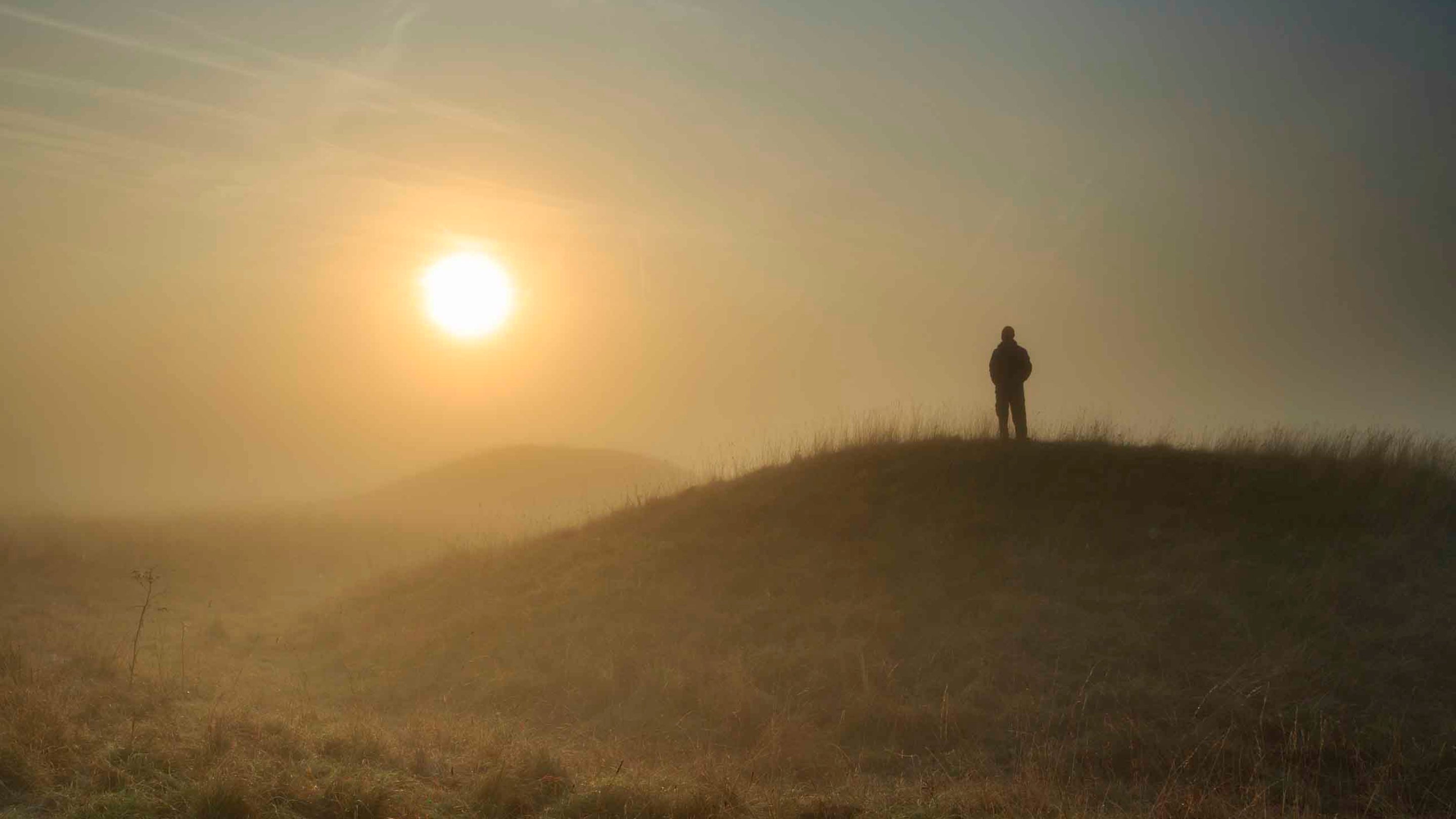 A person silhouetted against orange sun at Cursus Barrows, Stonehenge Landscape