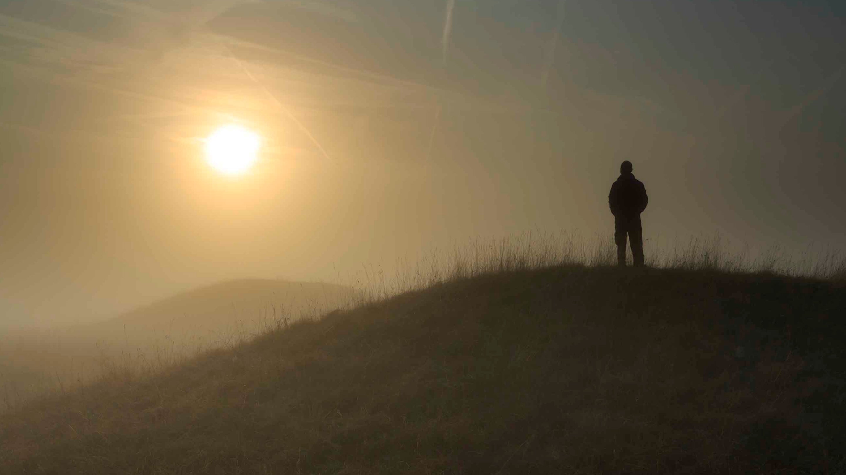 A person silhouetted against sunrise at Cursus Barrows, Stonehenge Landscape.