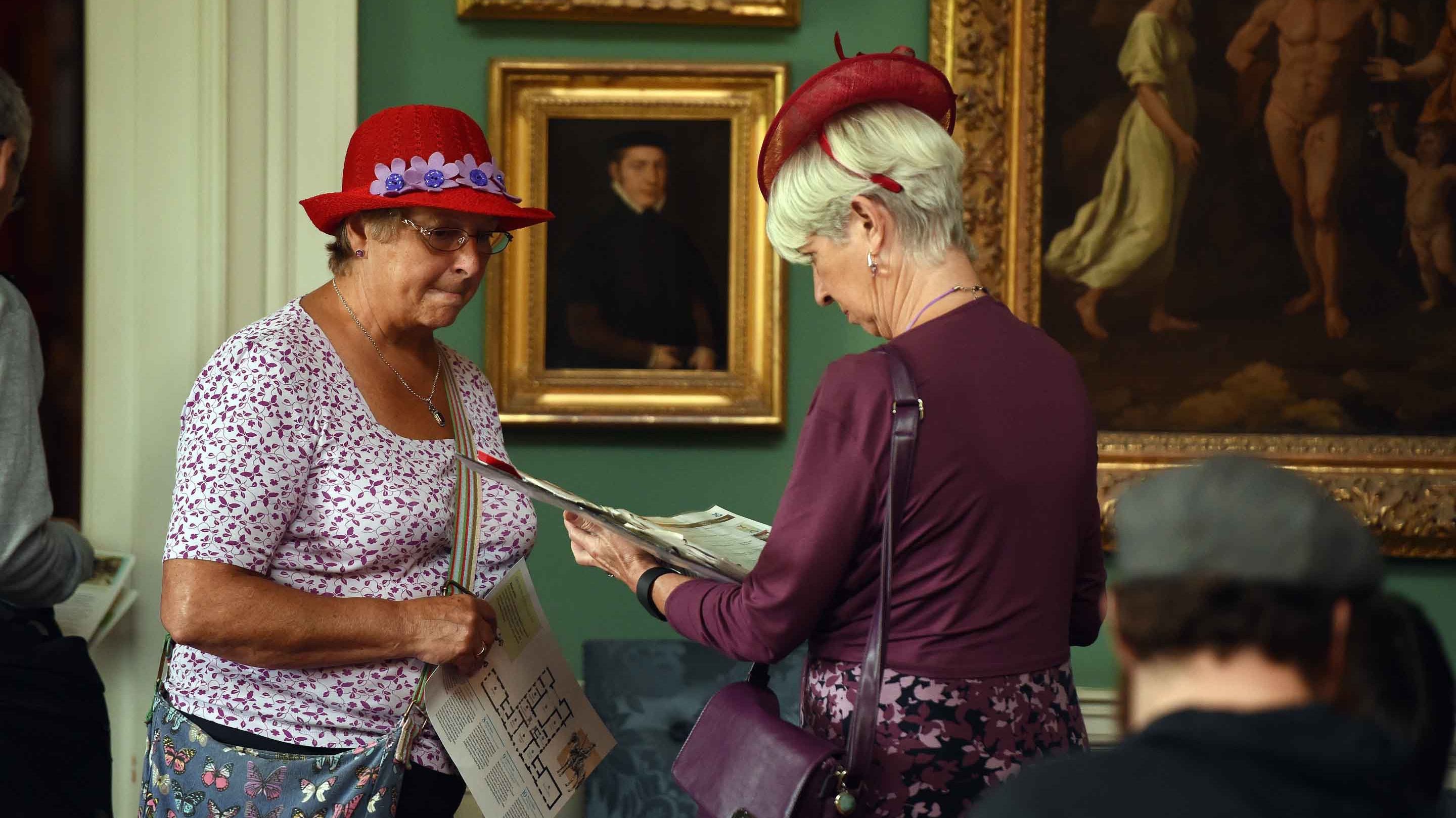 Two visitors look at a pamphlet in the Picture Gallery inside the house at Stourhead, Wiltshire