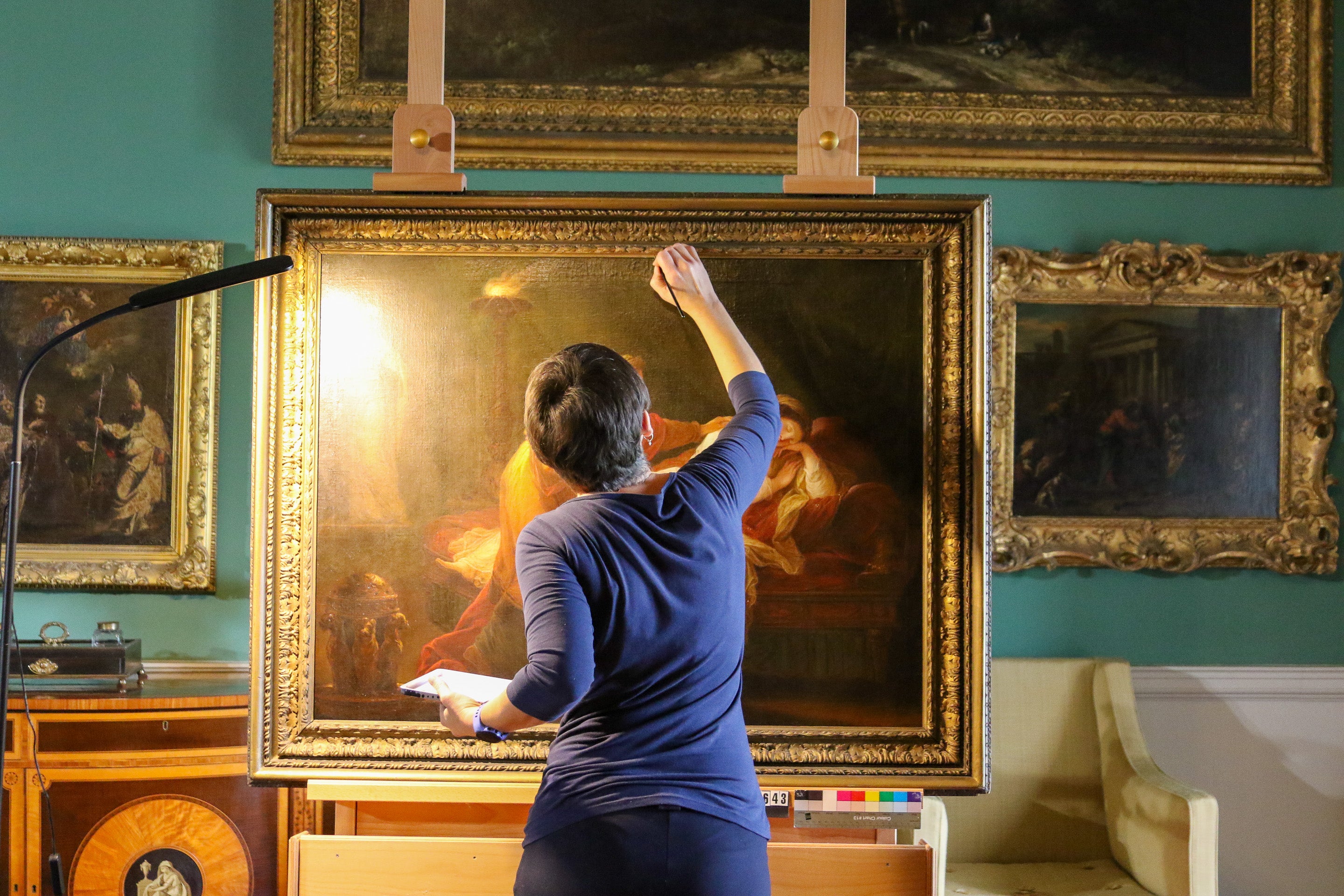 Conservator April Johnson applies touch up paint to the fine oil painting 'Penelope and Euriclea' by Angelica Kauffman displayed inside the picture gallery, Stourhead, Wiltshire