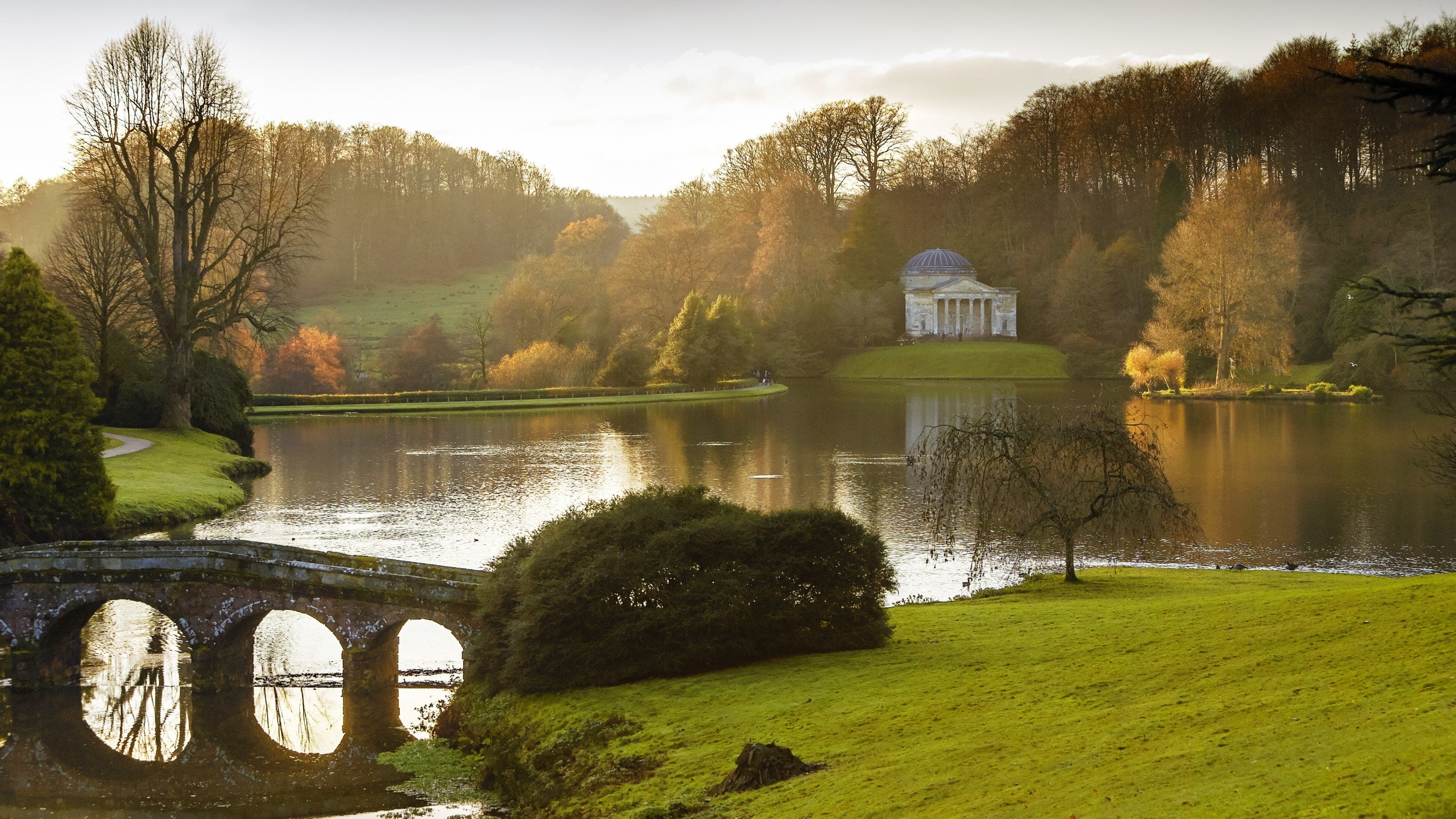 A Grecian-style structure on a small hillock across a lake in winter light