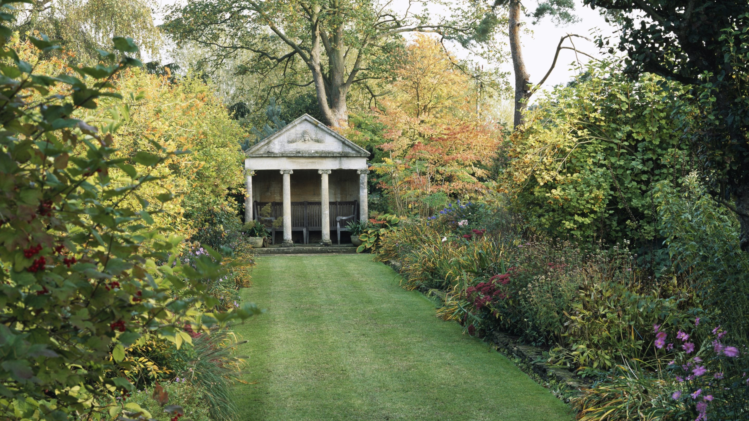 A stretch of lawn leading up to The Temple at The Courts Garden with autumnal borders and trees either side in Wiltshire.