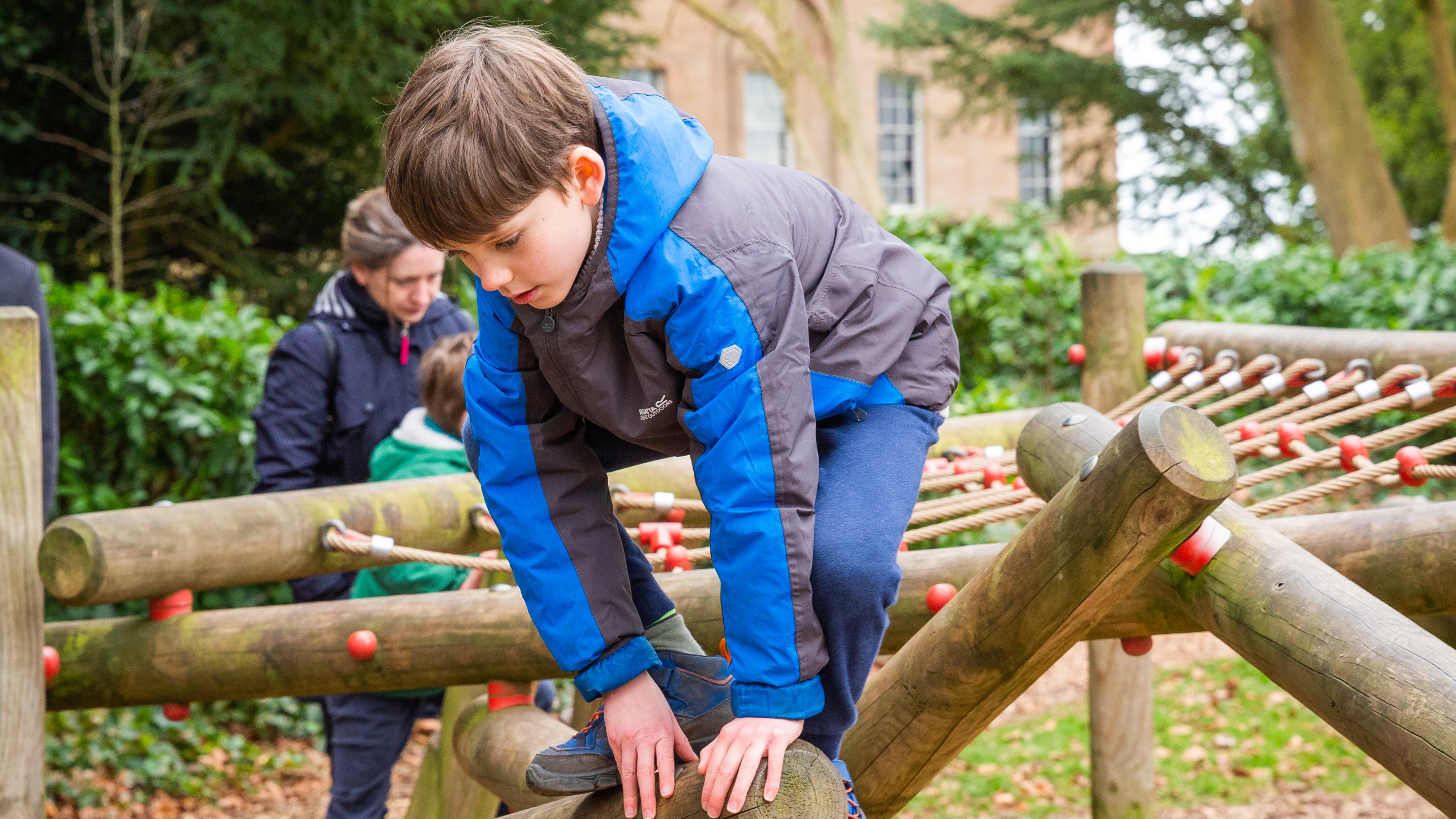 A boy climbing on a rope play area with the mansion out of focus in the background.