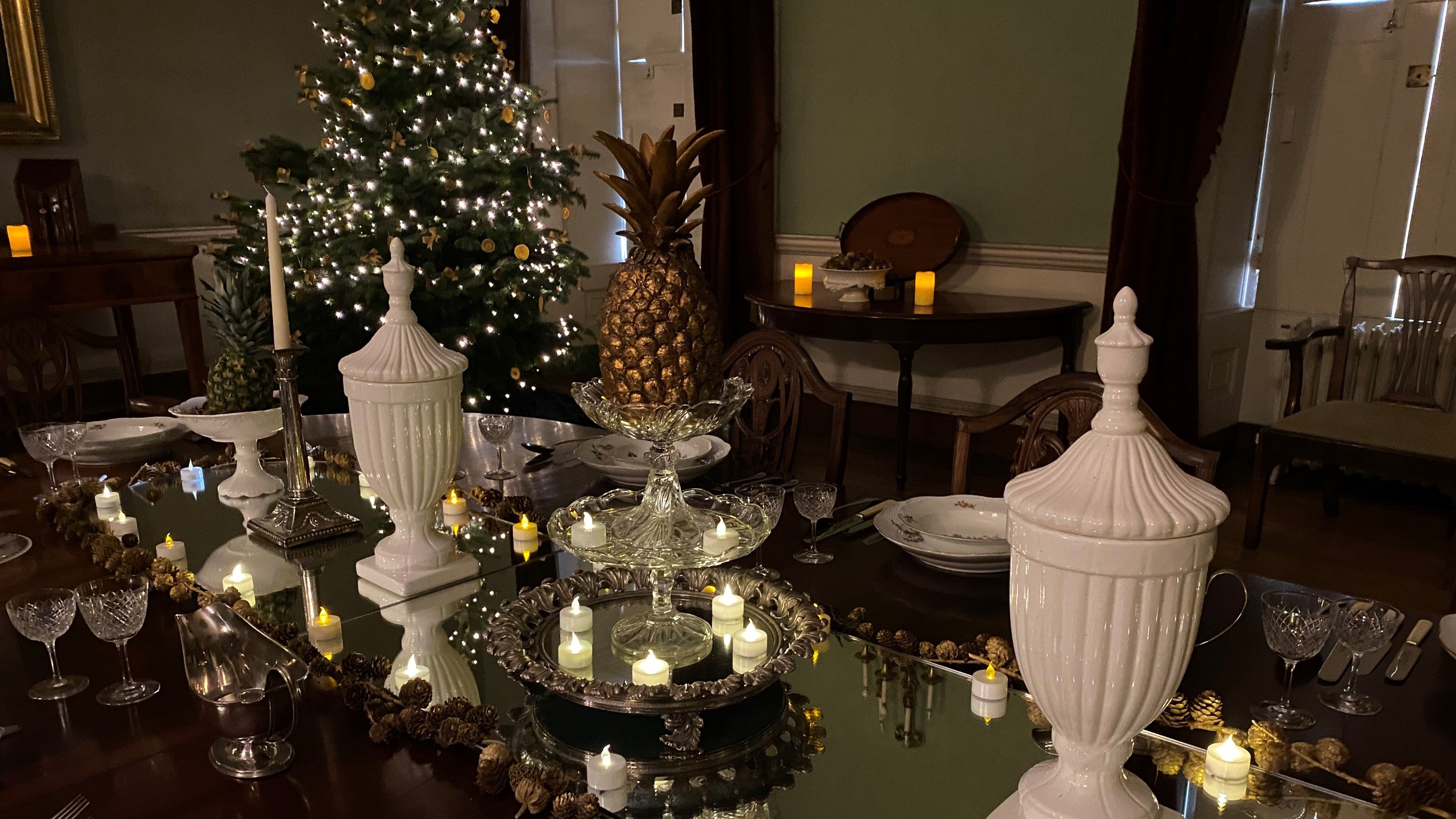 A gold pineapple in the centre of a decorated dinging room table, lit with small candles and a Christmas tree in the background