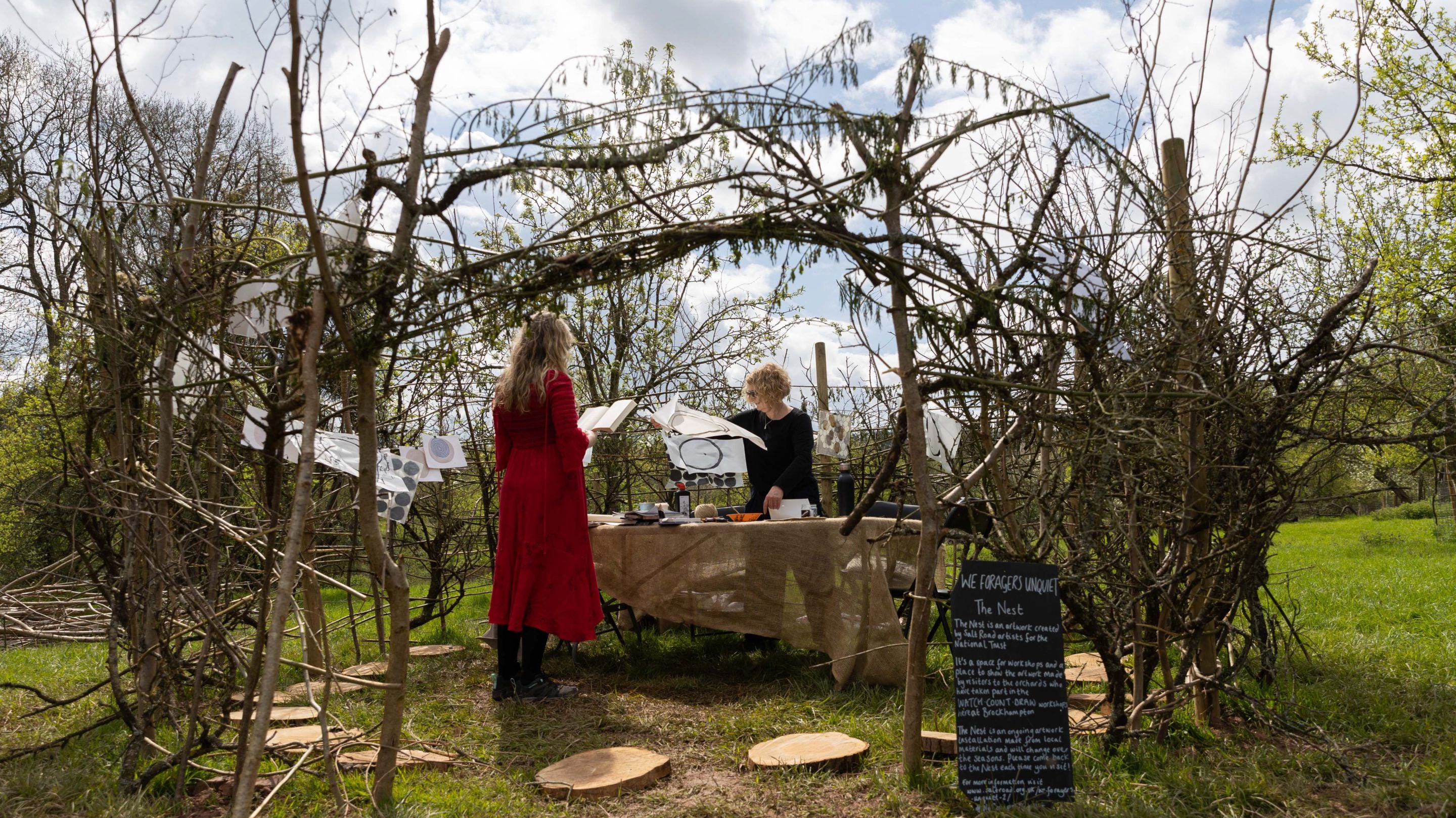 Two people standing around a table within the 'nest', which is a tall circular space made from large sticks to look like a giant birds nest to