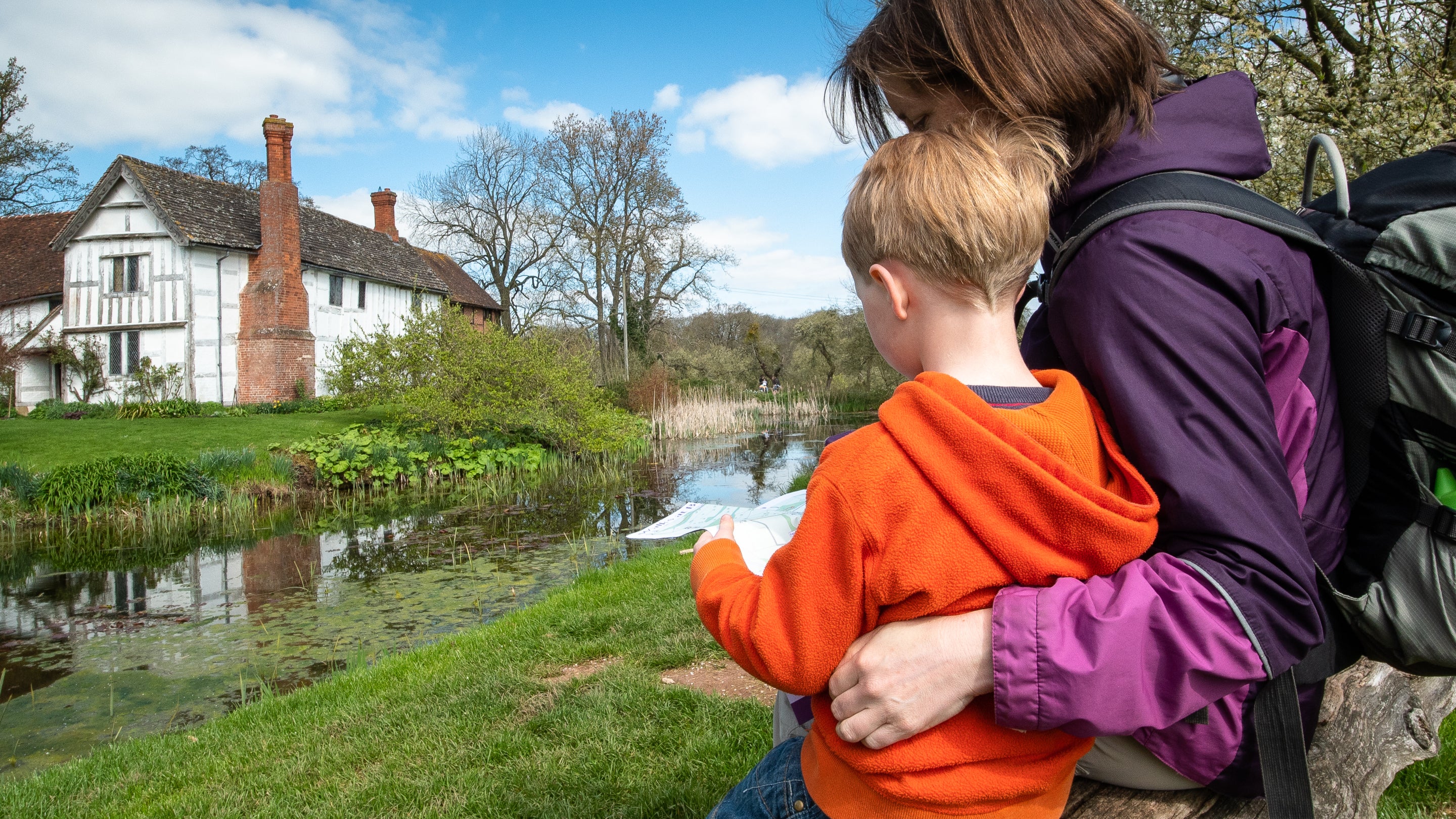 A mother and child sit on a bench overlooking the manor house.