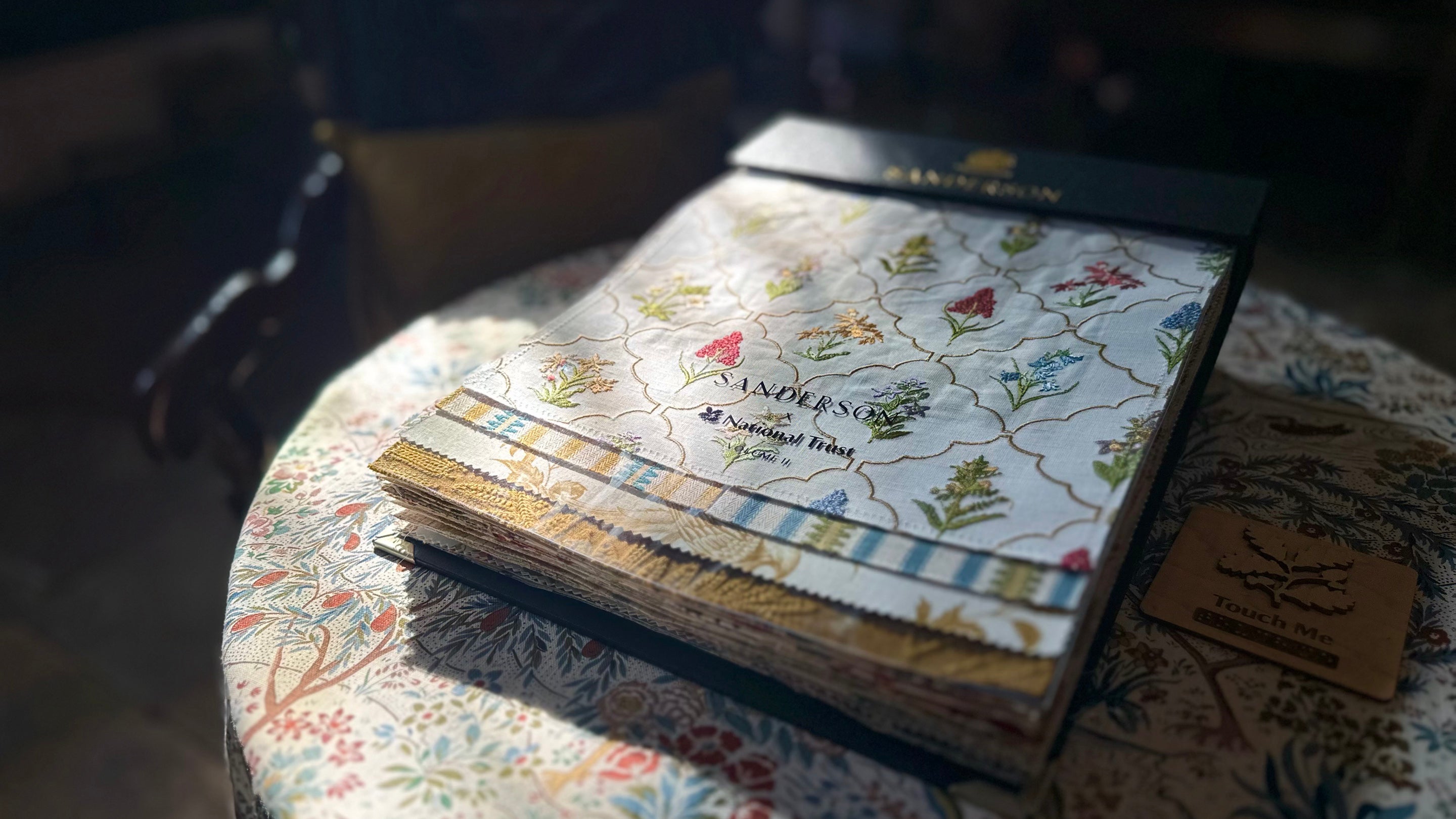 A Sanderson fabric book showing the Brockhampton inspired collection. It sits on a table with light gently falling on the book.