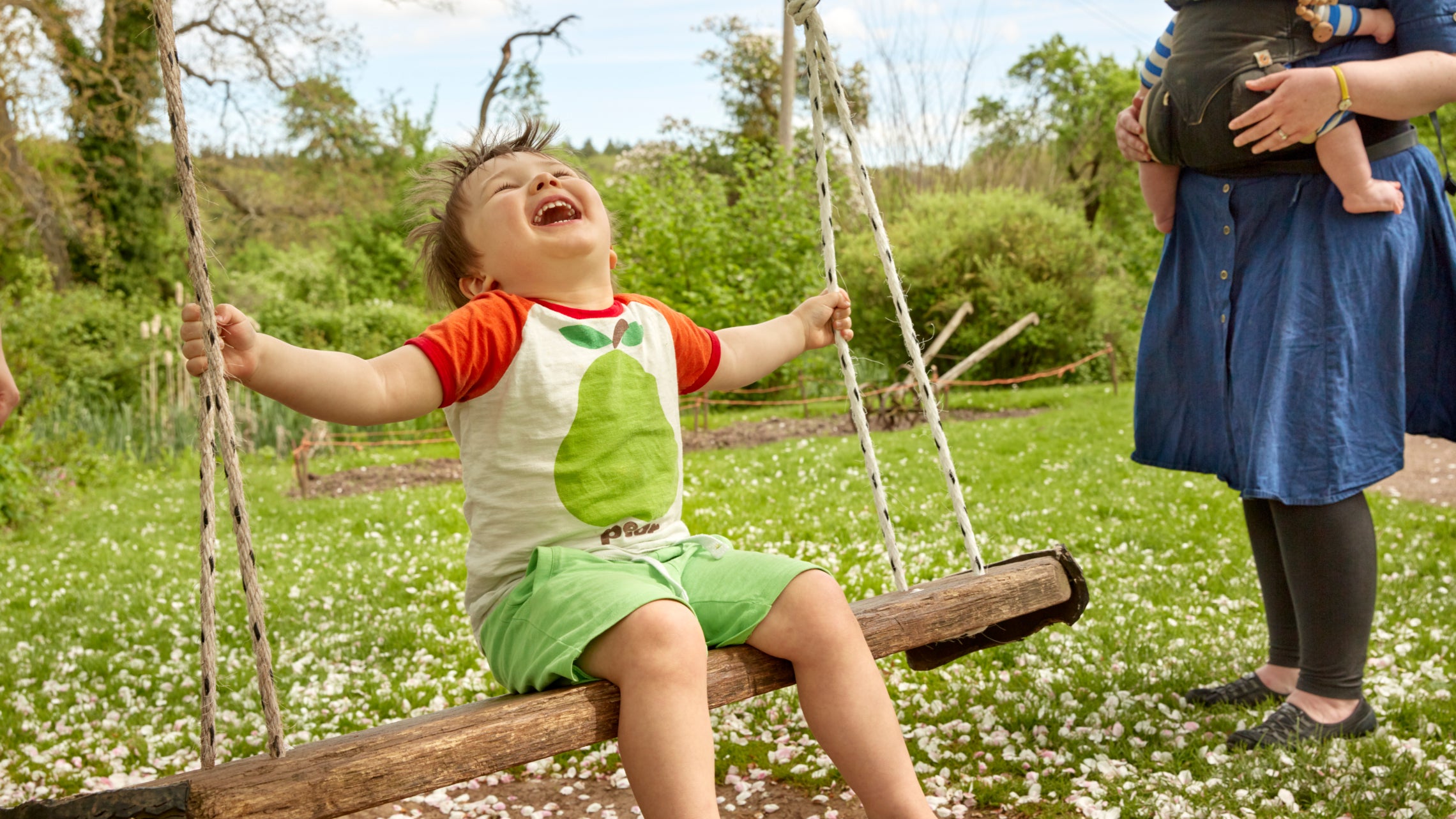"A young boy joyfully swings in the park, his father pushing him high into the air, while his mother tenderly carries a young baby nearby at Brockhampton.