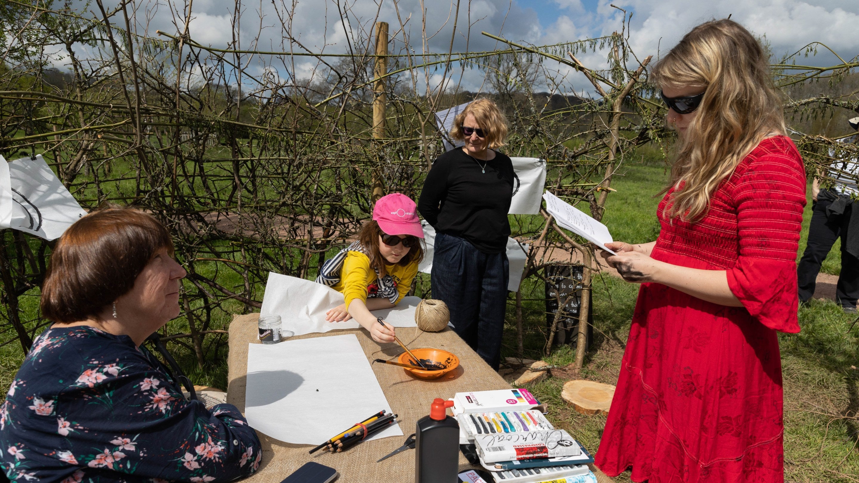 Three women and a child outside, surrounding a table with painting and art supplies.