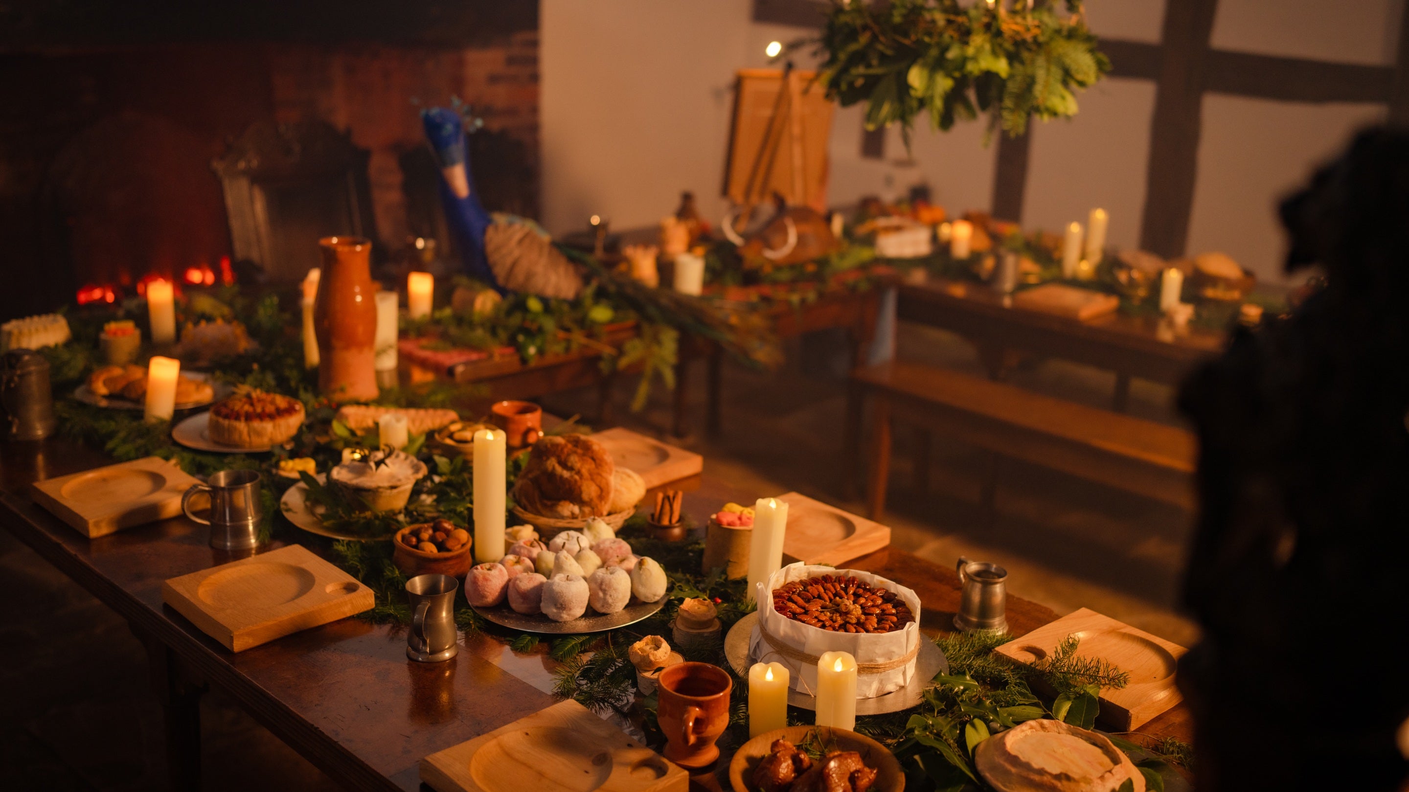 A 'U' shaped table adorned with artifical foods, greenery, candles, plates, tankards, and a giant felt peacock.
