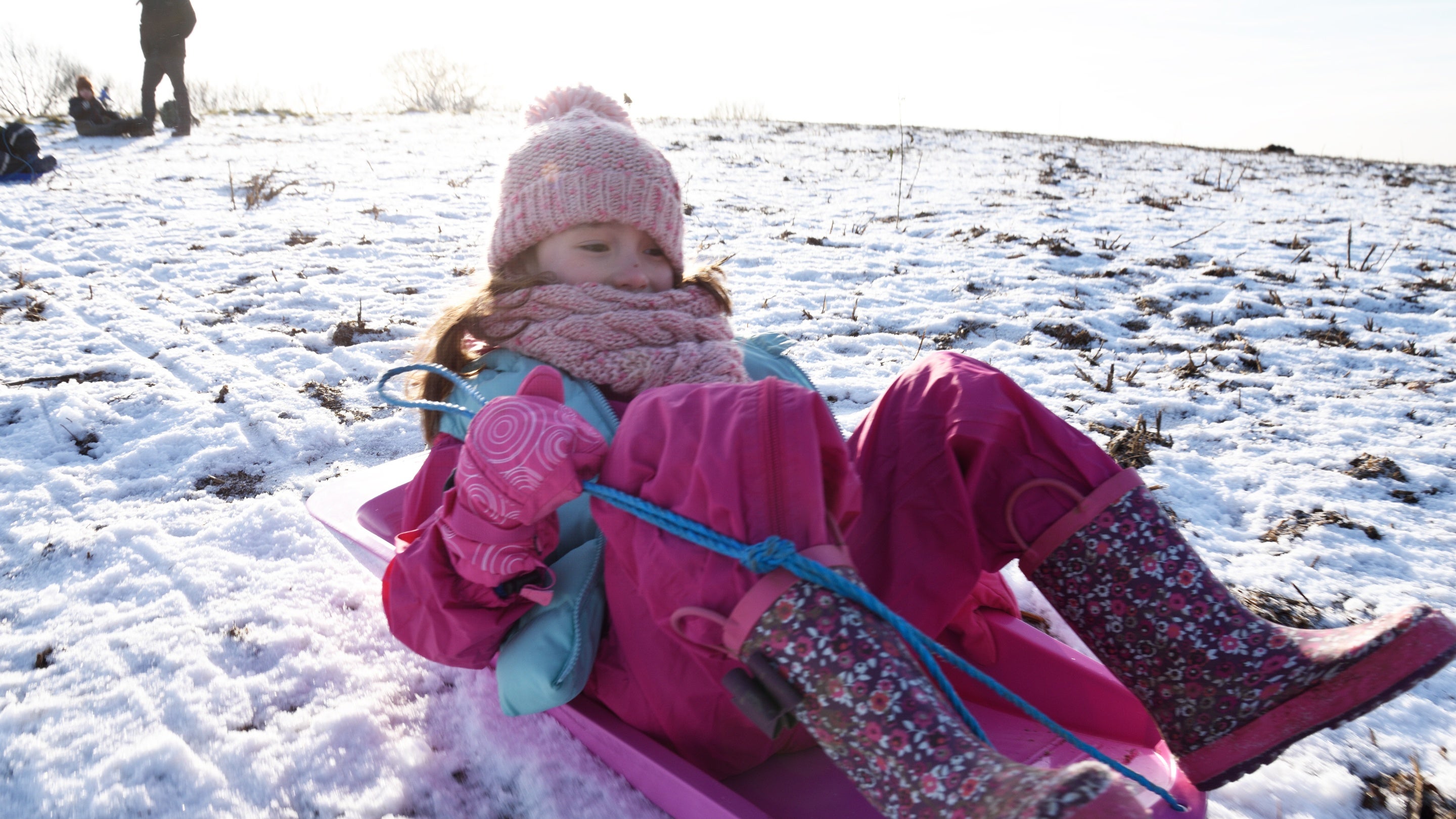 A child wrapped up in winter clothes sliding down a snowy hillside in a sled at Clent Hills, Worcestershire