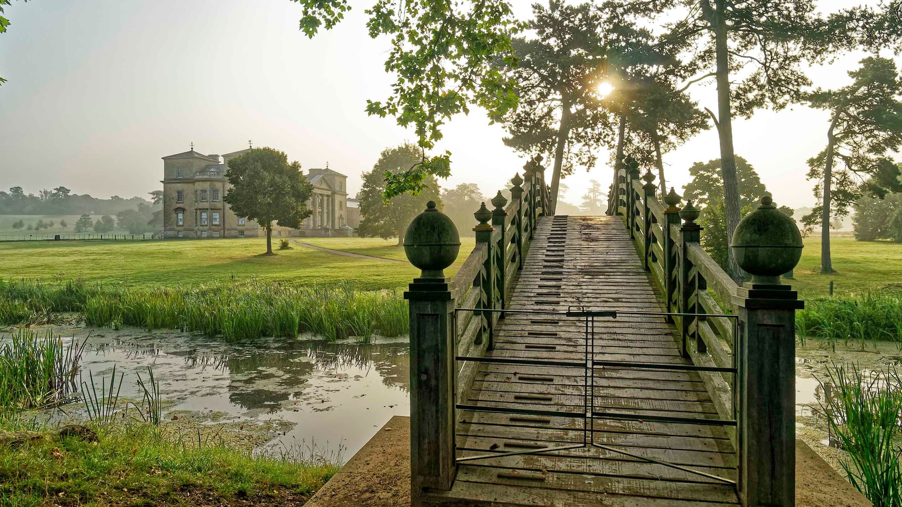 The Chinese Bridge over the river in the park with the Palladian mansion in the background at Croome, Worcestershire
