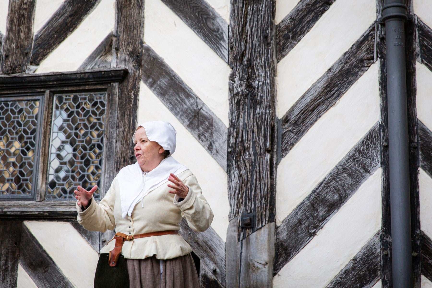 A Tudor reenactor holding a demonstration outside a timber-framed house