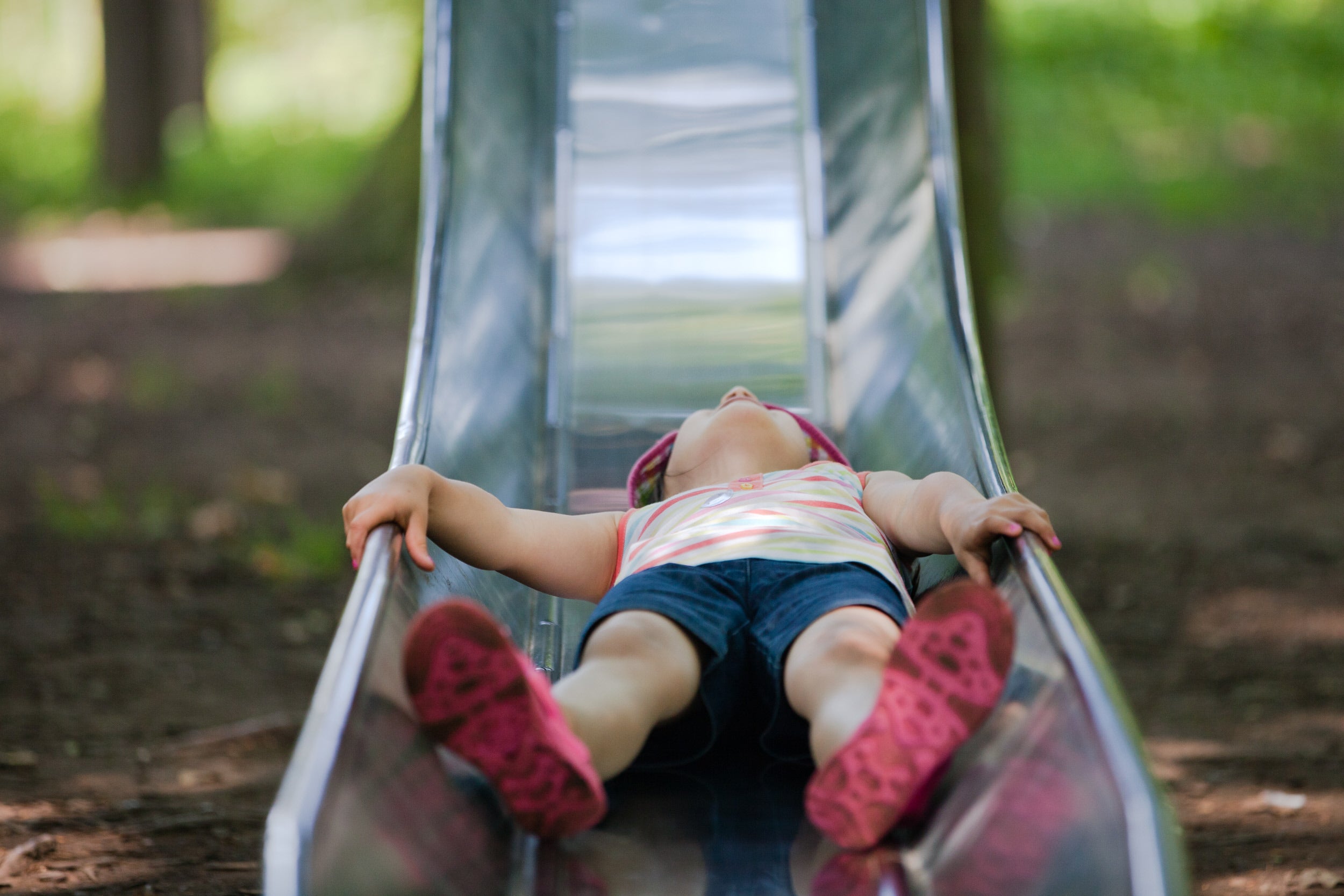 A little girl sliding down a metal slide in a playground