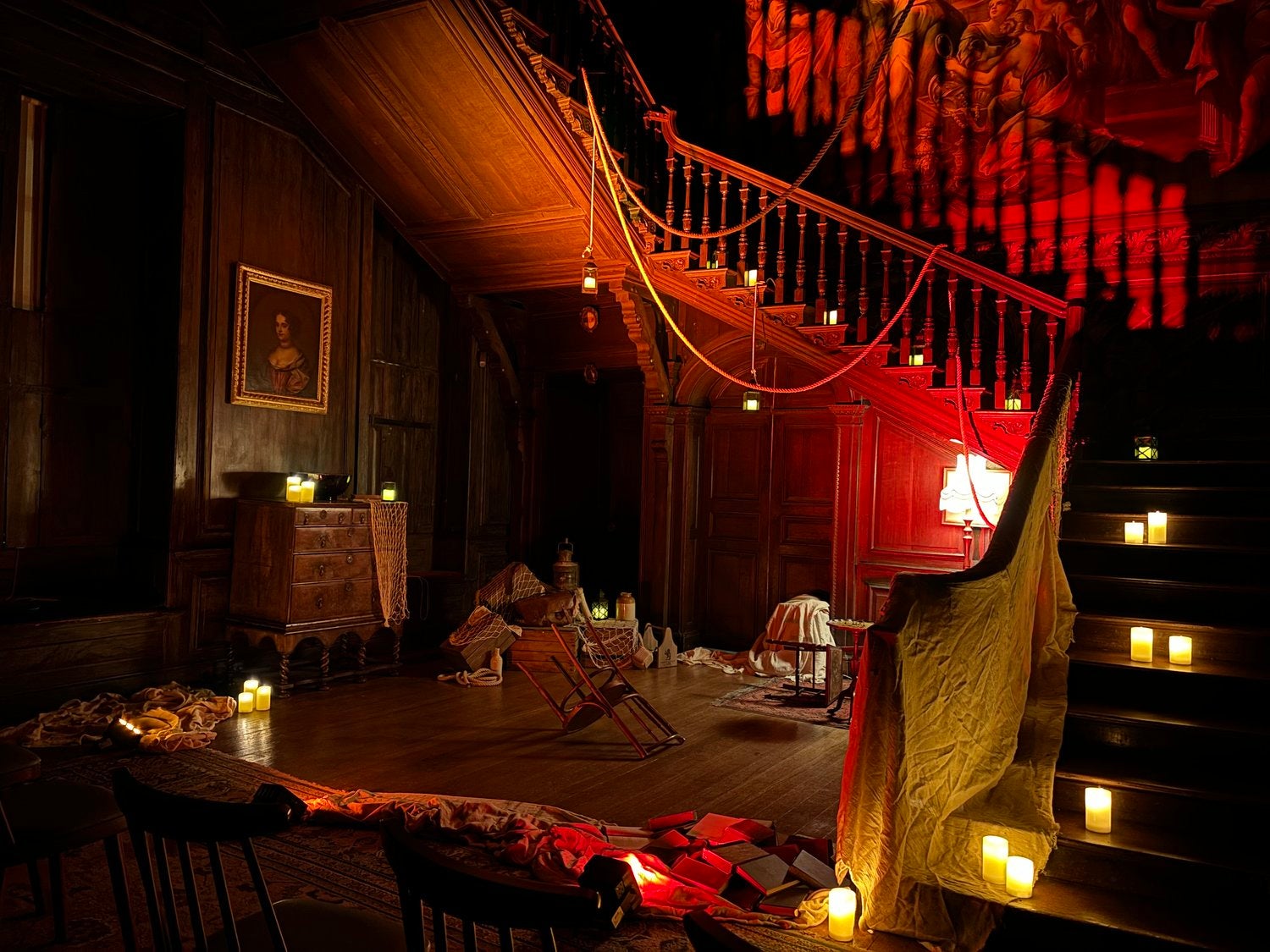 The Great Hall inside Hanbury Hall lit up with red light and set for a ghost story including candles, sheets, crates and old furniture