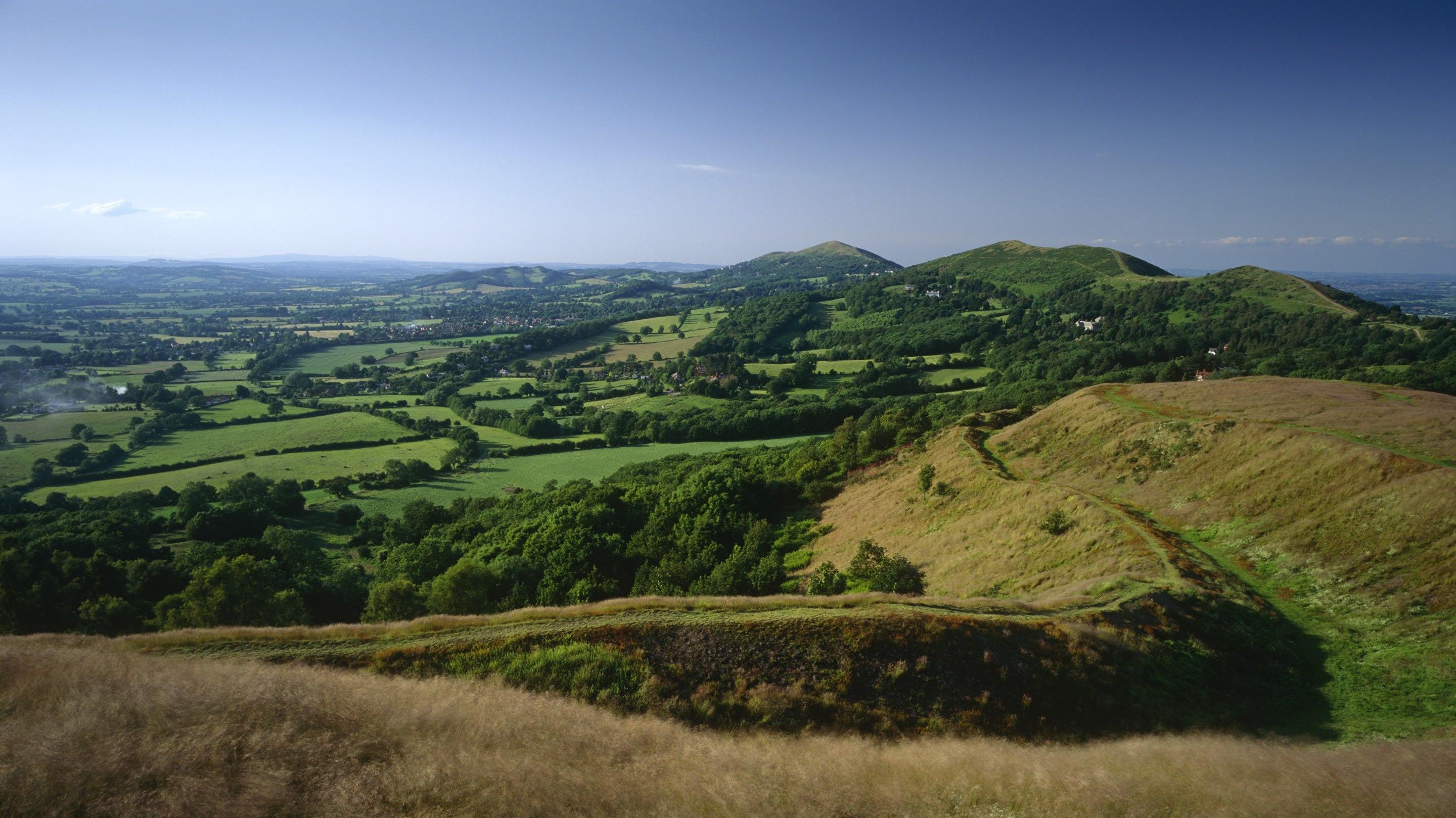 Wide view of the Malvern Hills, showing the escarpment and the path in the foreground and the Worcestershire Beacon beyond.