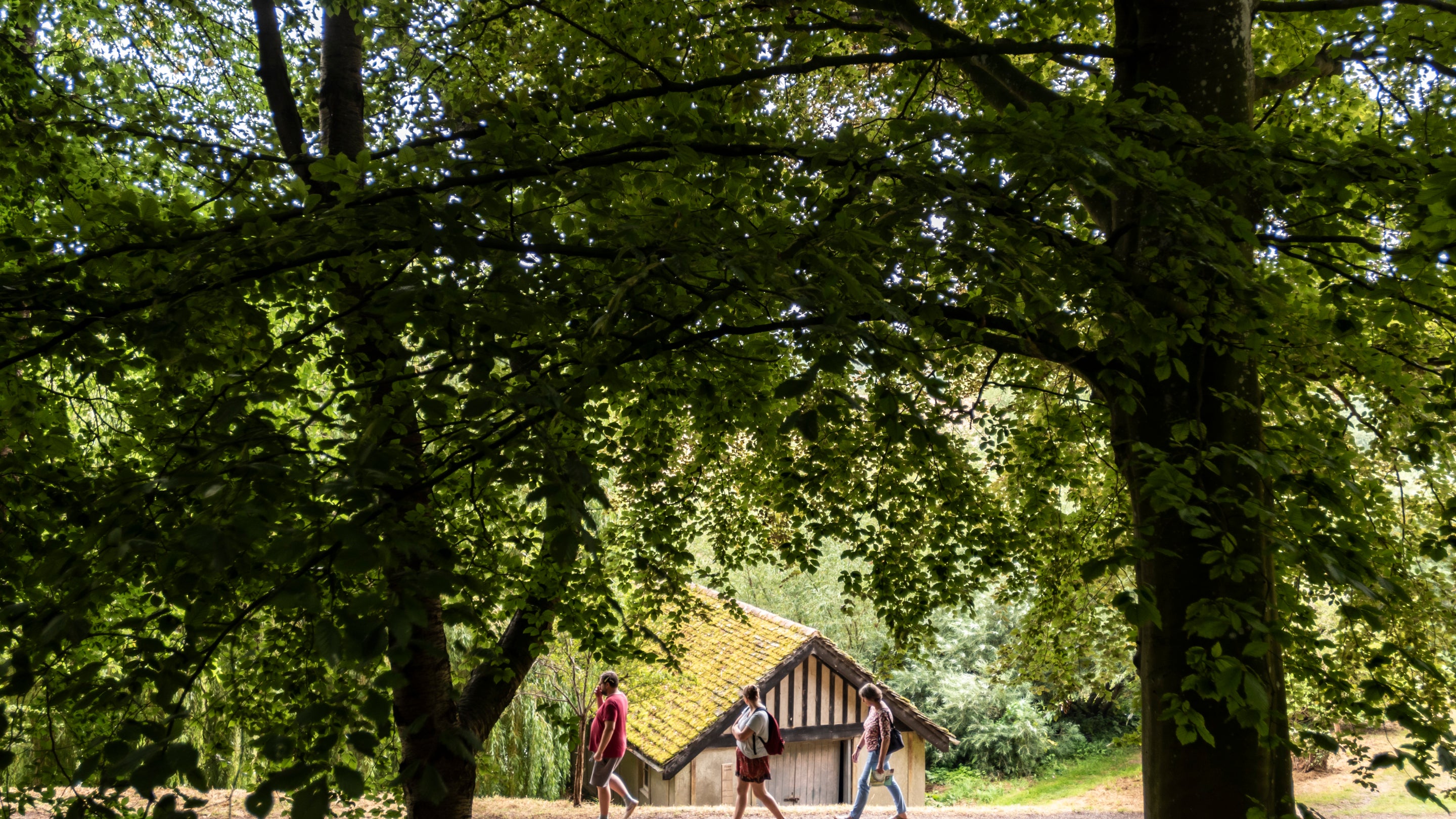 A long distance shot of two visitors walking past the boathouse in the garden.