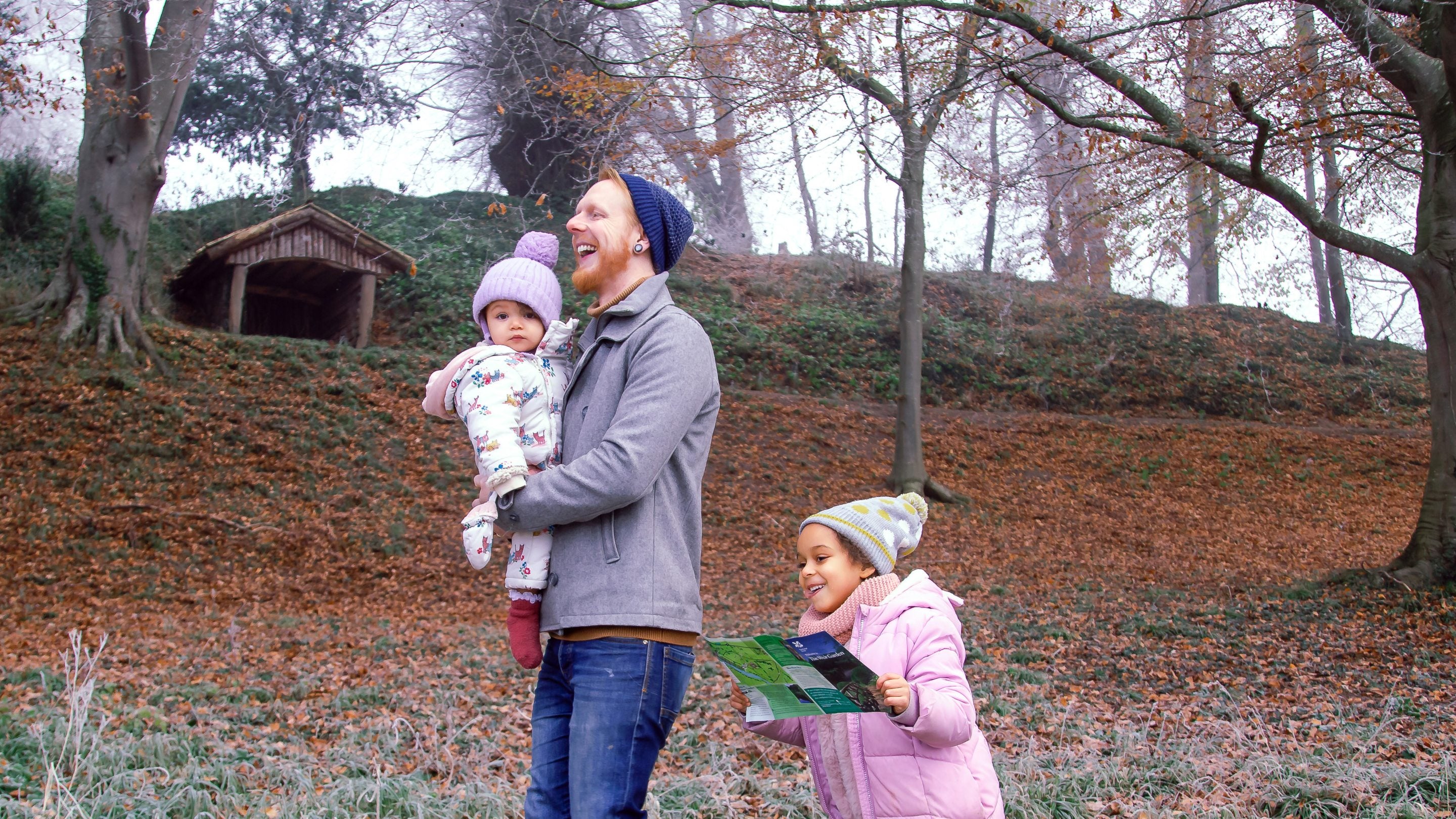 ather holding a baby laughs while walking beside a small child holding a map. In the background, frost and winter trees cover the Weir Garden.
