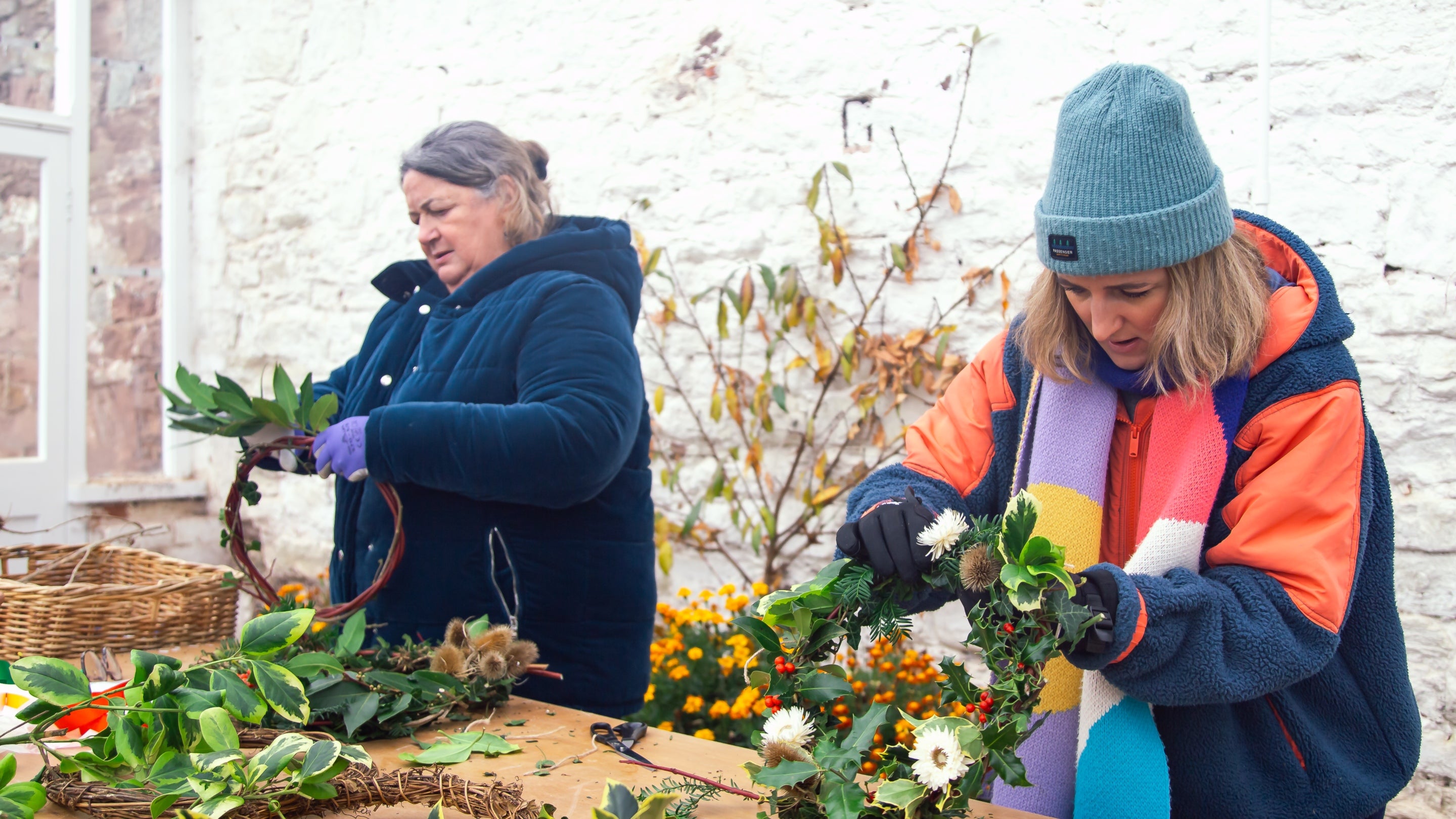 Two women crafting a Christmas wreath at the glasshouse in The Weir Garden