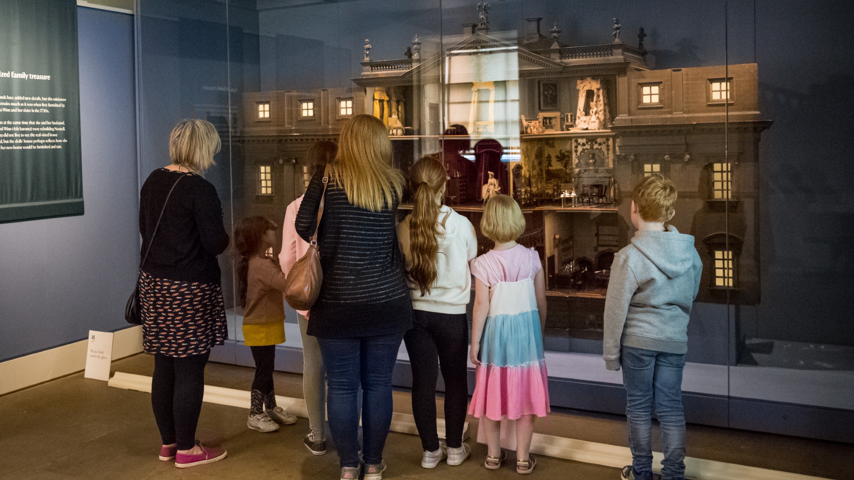 Family looking at a miniature dolls house behind a glass case