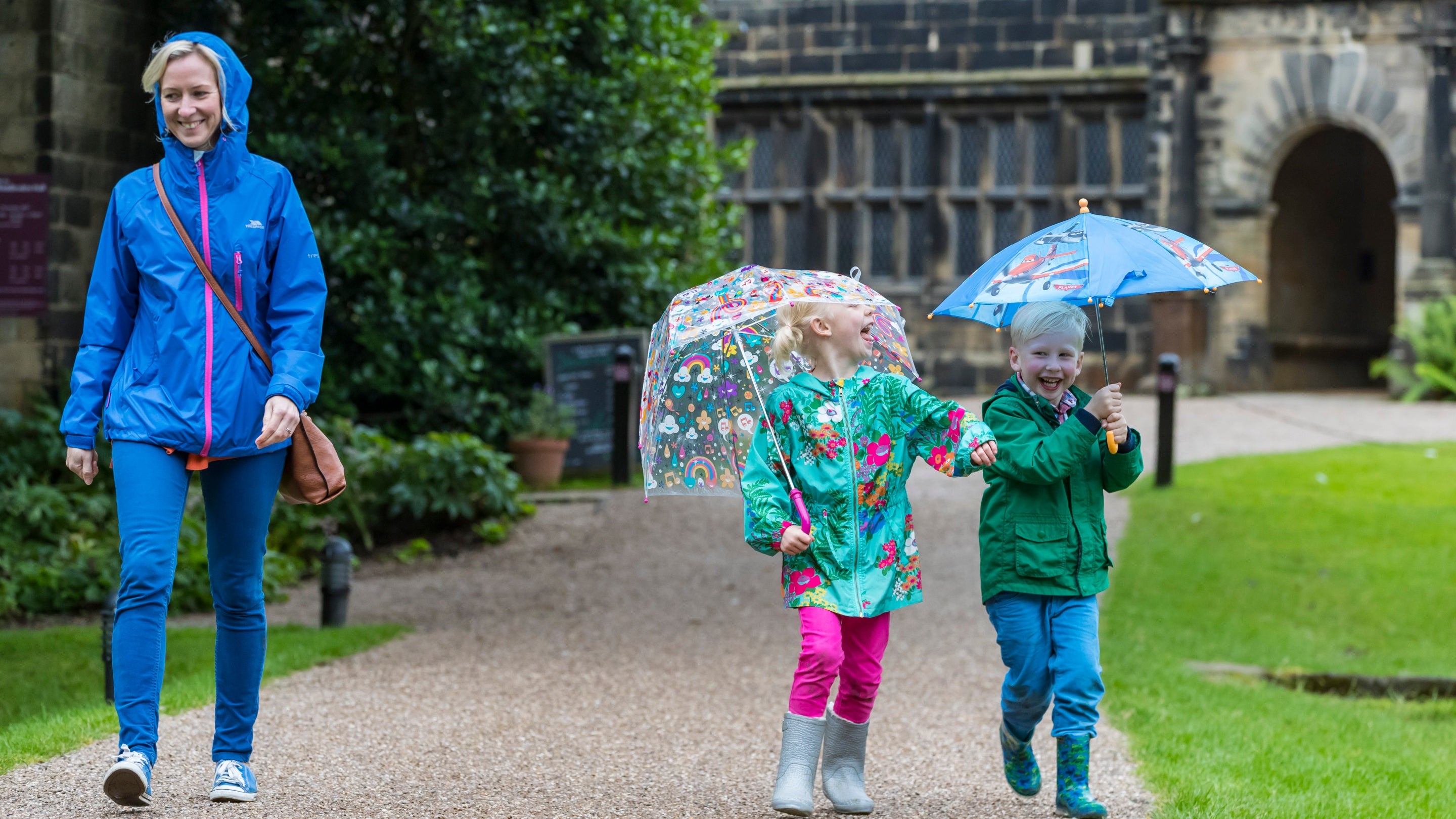 Two children with umbrellas and a woman smiling with her hood up
