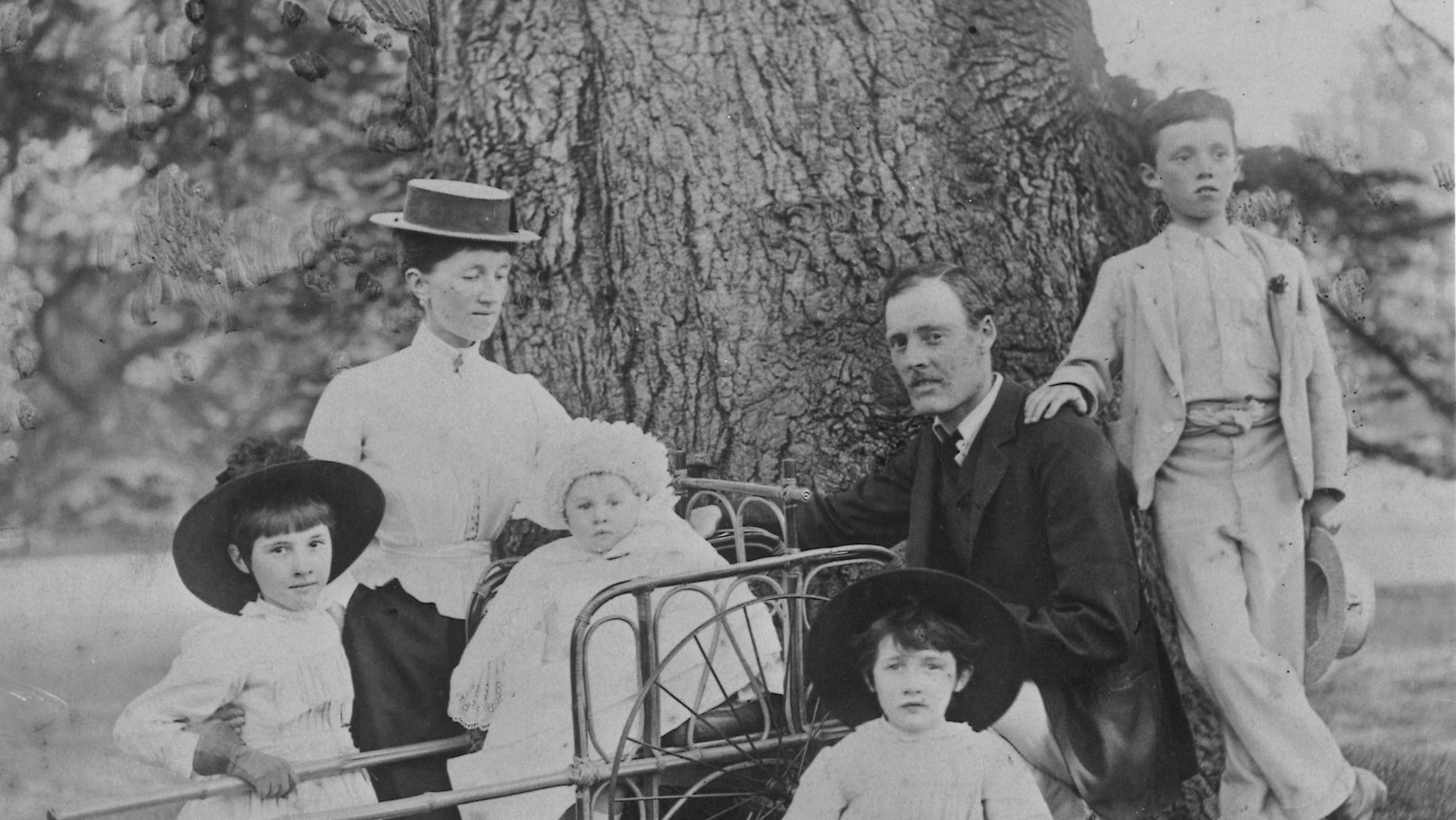 Black and white photograph of a family in a garden near a large tree trunk