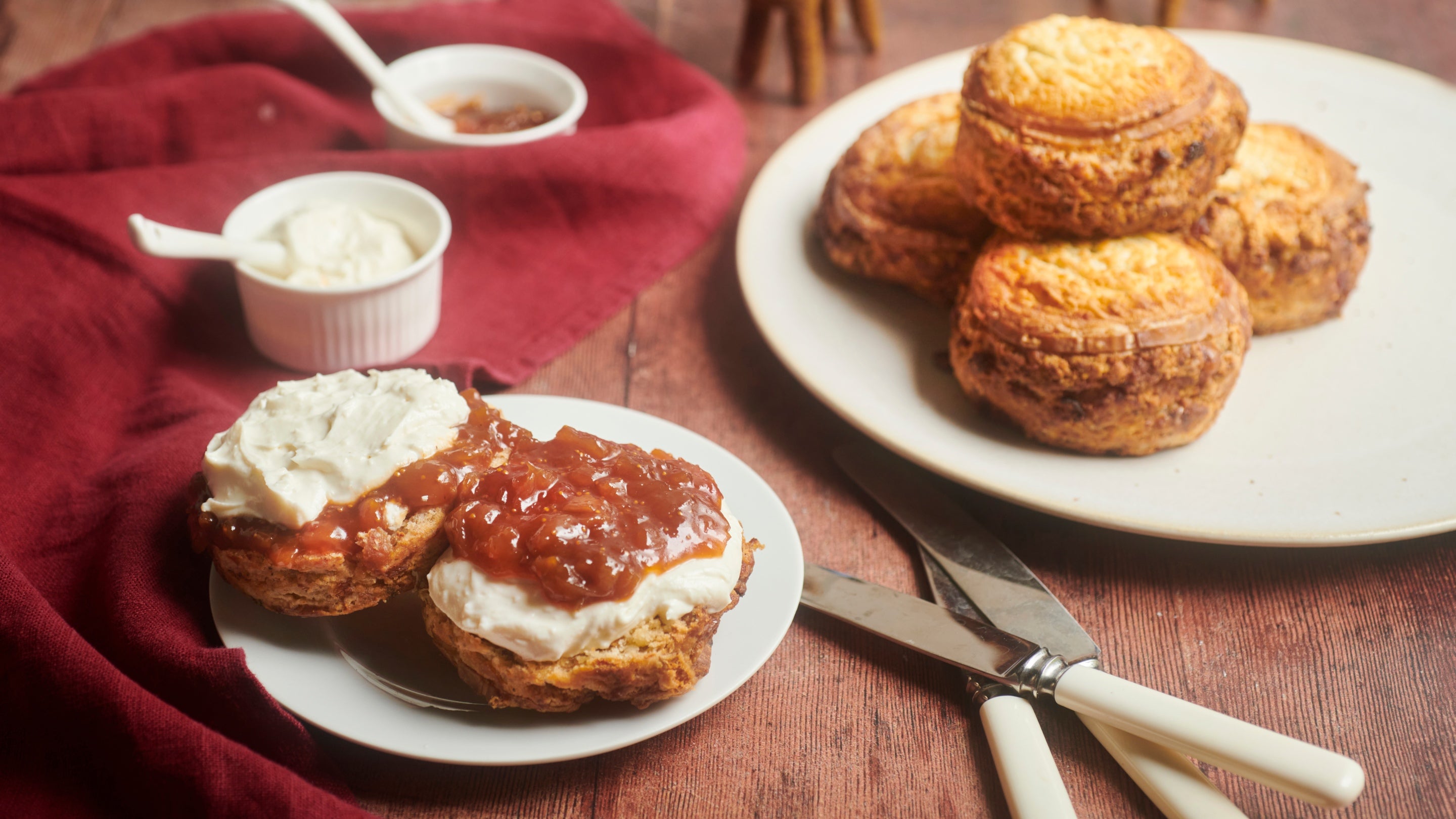 Scones on two plates, one open with goats cheese and fig chutney spread over and more in small pots