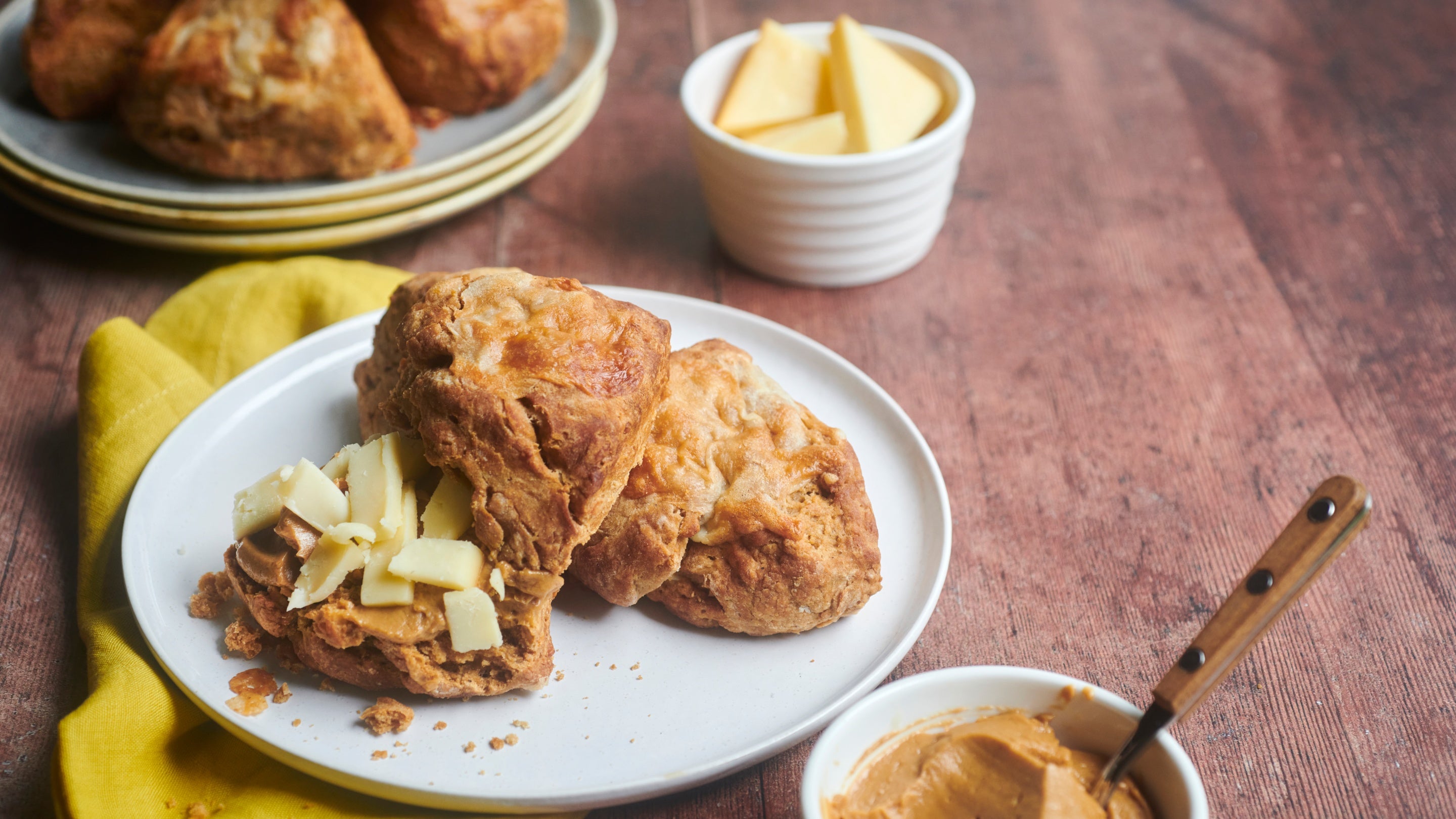 Scone on a plate, one with a spread and small pieces of cheese on top