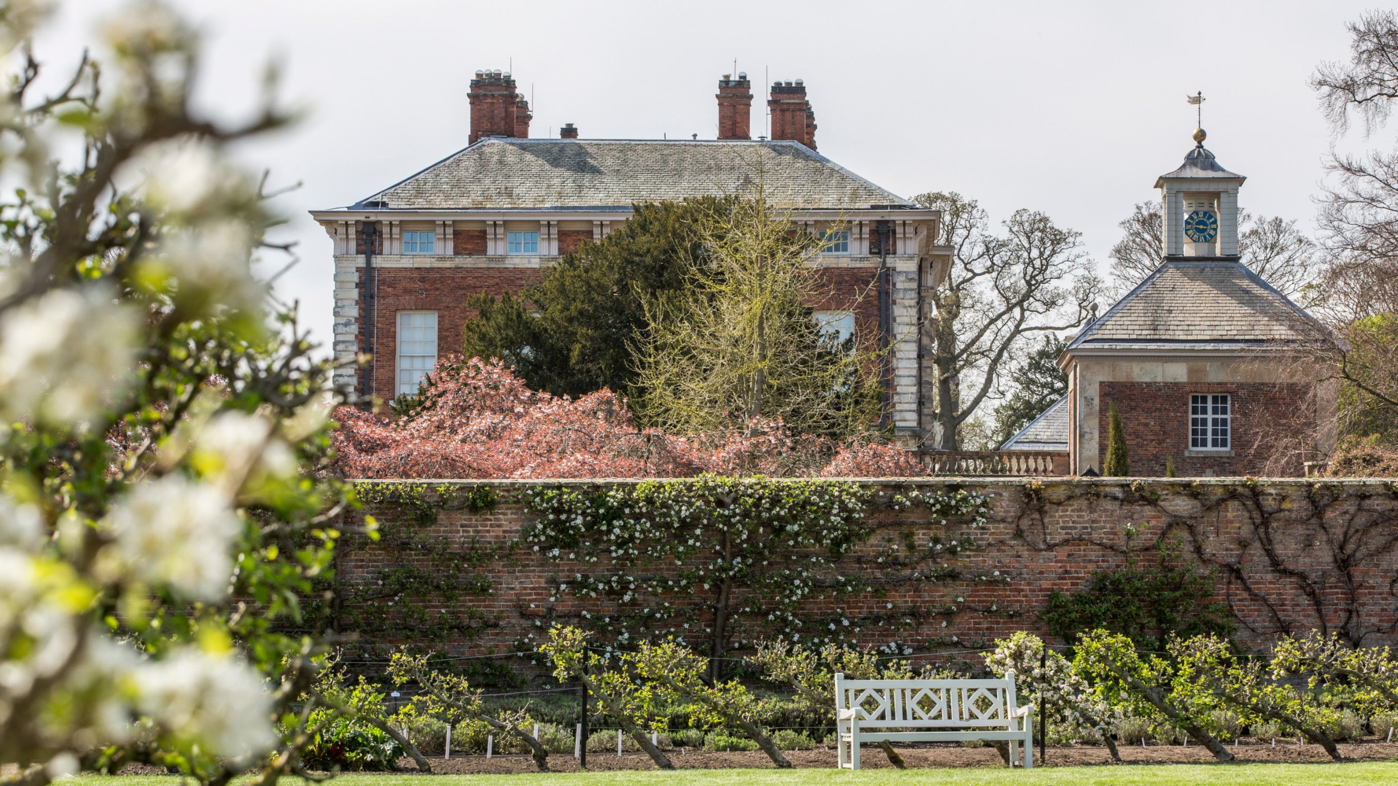 View of the east front and bell tower at Beningbrough with white and pink blossom on the trees