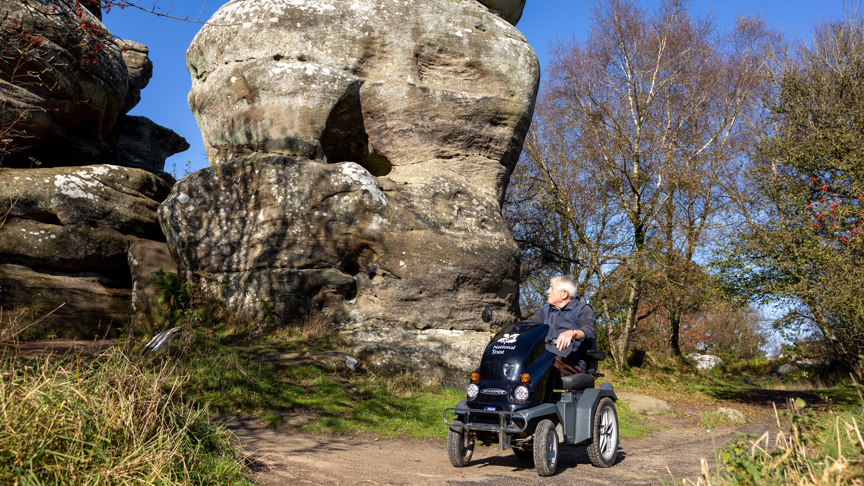 Man sat on a black mobility scooter travelling along the accessible path with a large rock formation in the background