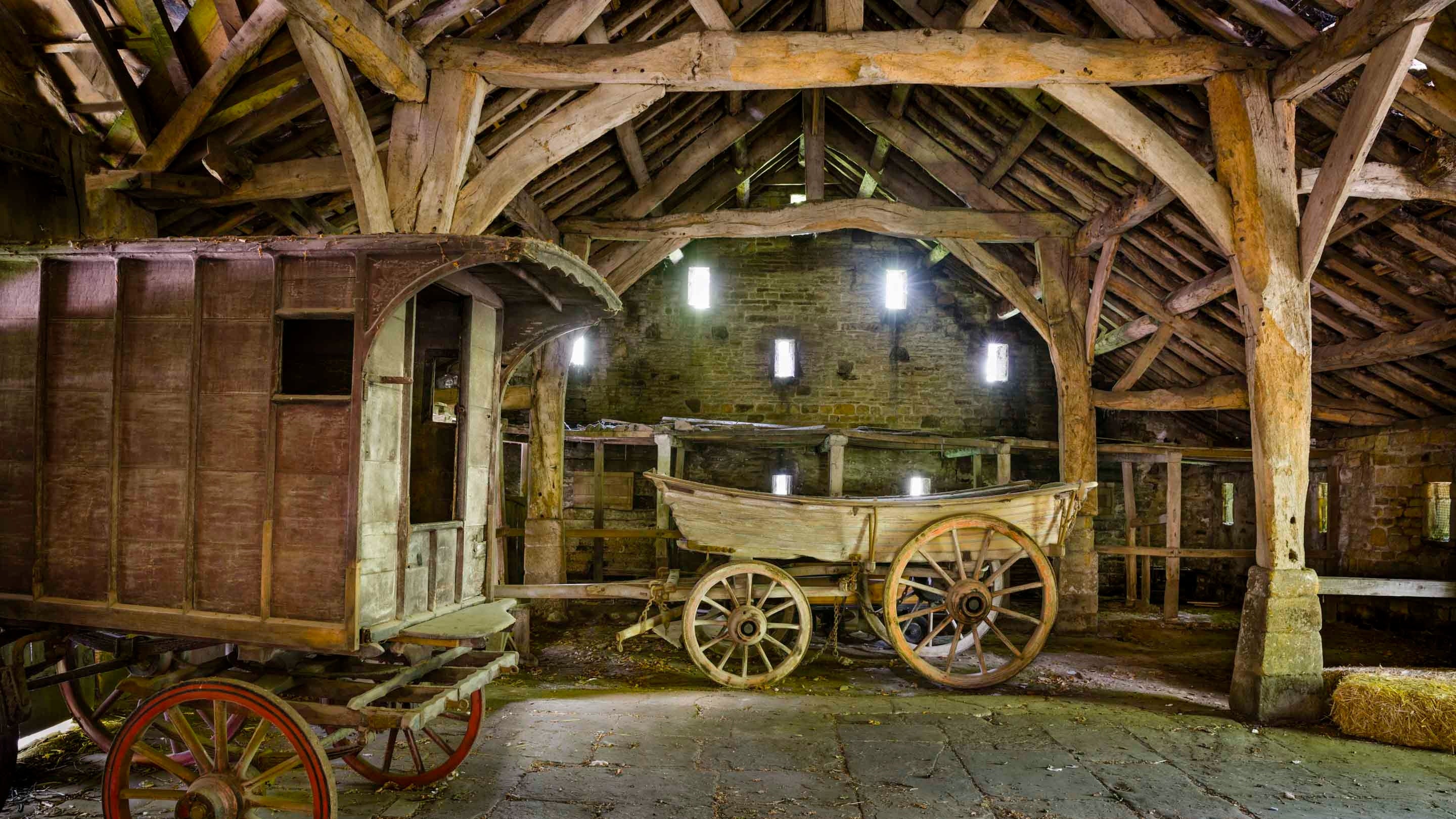 The interior of the Great Barn at Riddlesden Hall, showing its timber structure and containing historic wooden wagons