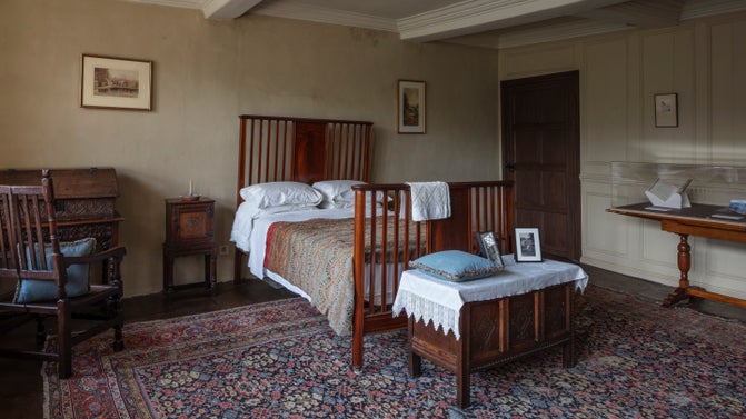 A 19th century bedroom with wooden framed bed and a patterned rug on the floor