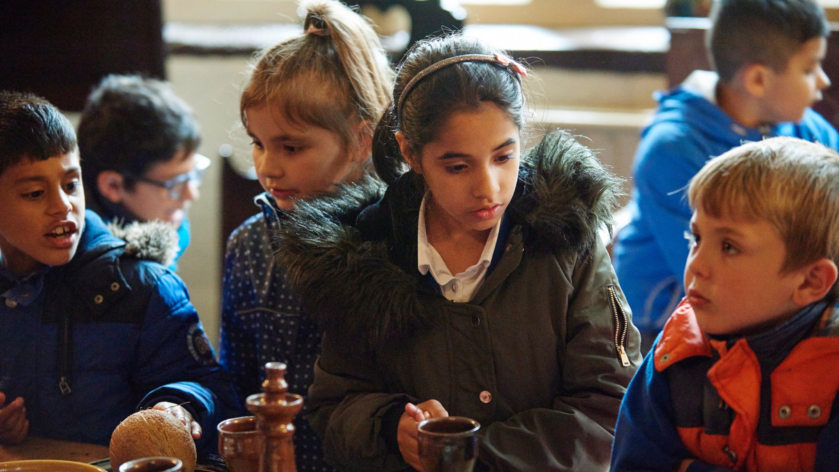 Close up of school children looking at wooden vessels on a table