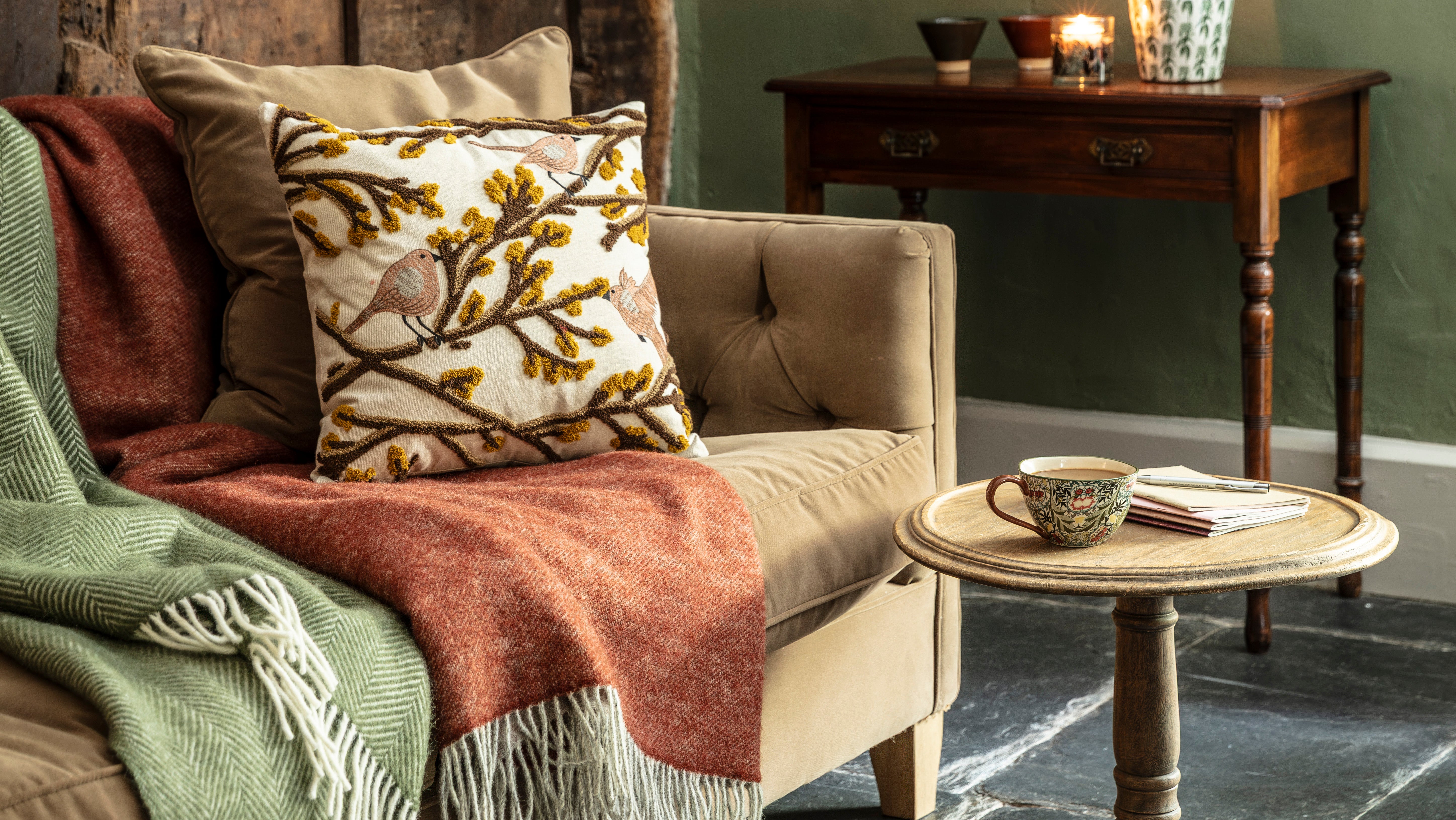 A sofa with two throws and an embroidered pillow next to a small table with a mug