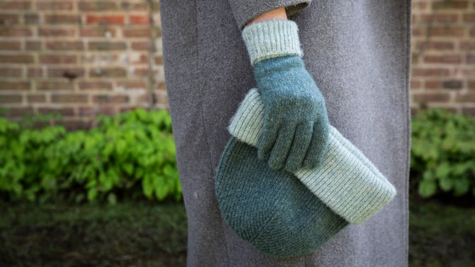 a gloved hand holding a matching green hat against a red brick background