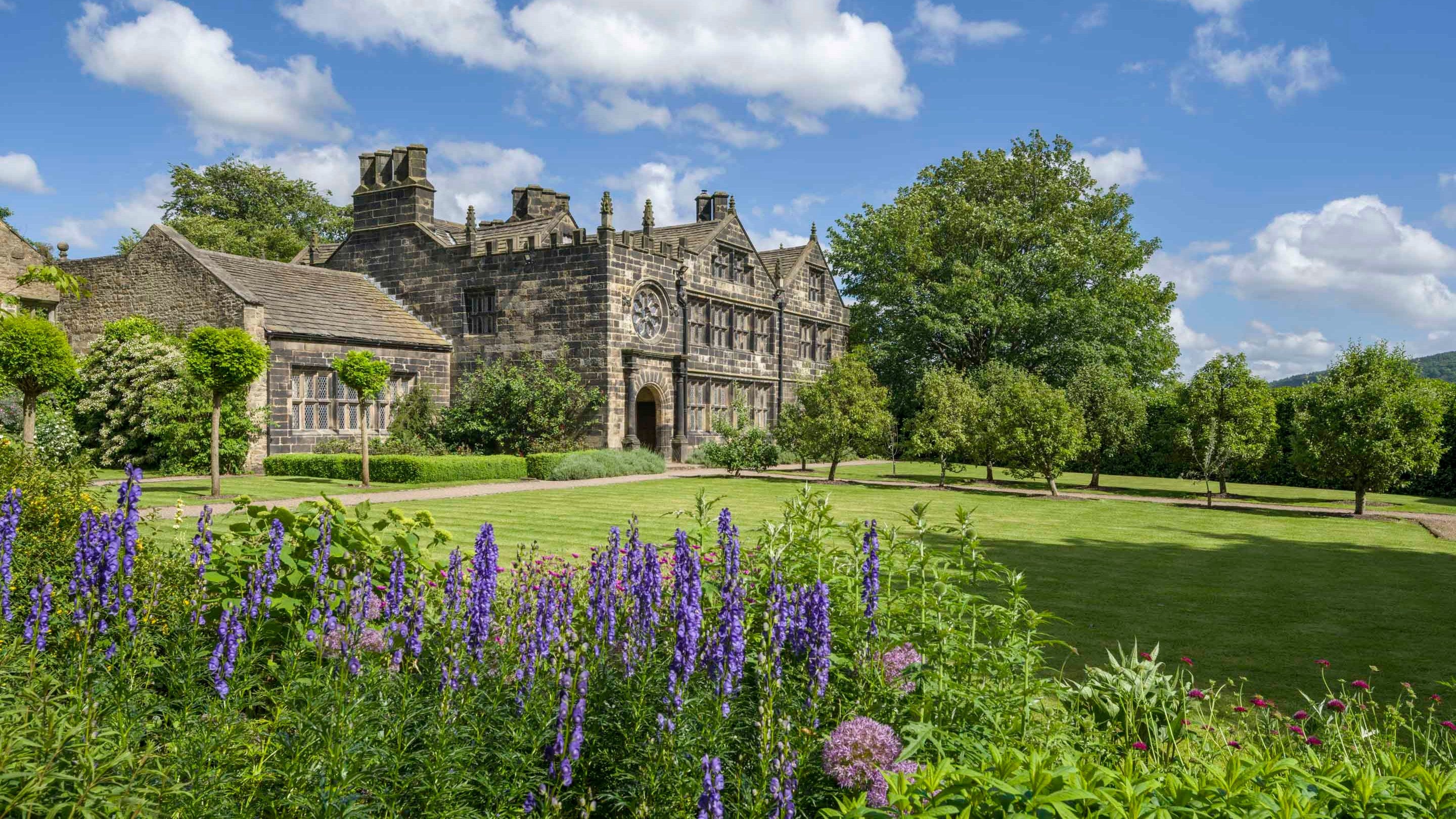 The south west front of East Riddlesden Hall in Yorkshire showing the Hall alongside trees, lawn and lavender