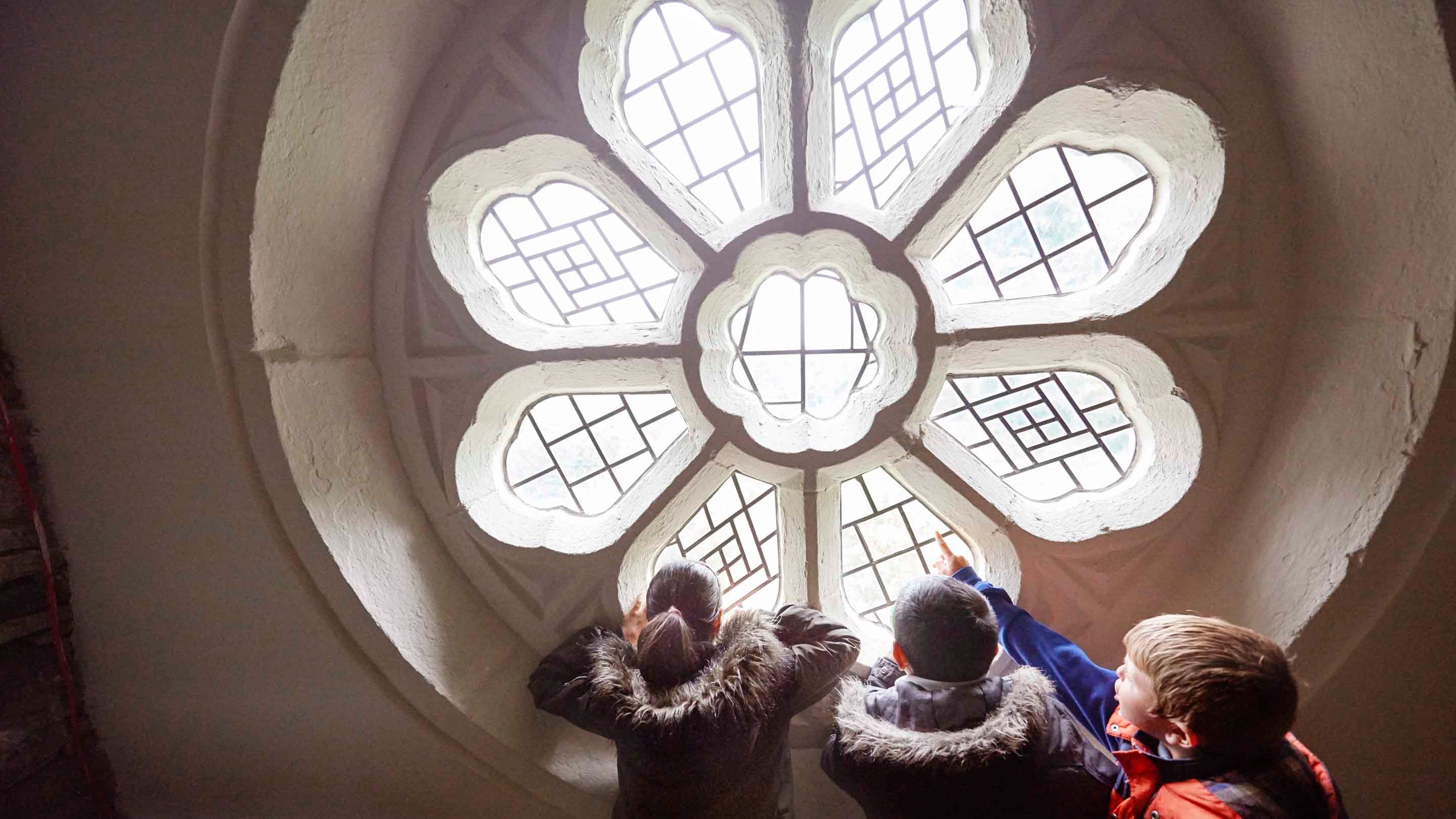 Three school children look through the rose window in the Yellow Porch Chamber at East Riddlesden Hall