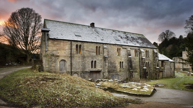 A frost covered ancient Mill in the foreground with bare trees and a fiery red sunset in the background