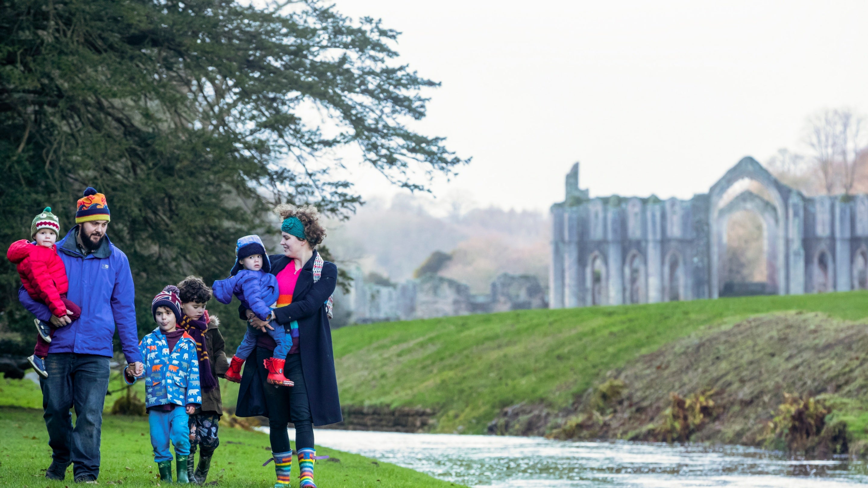 Family dressed for winter with a ruined arch and river of Fountains Abbey in the background