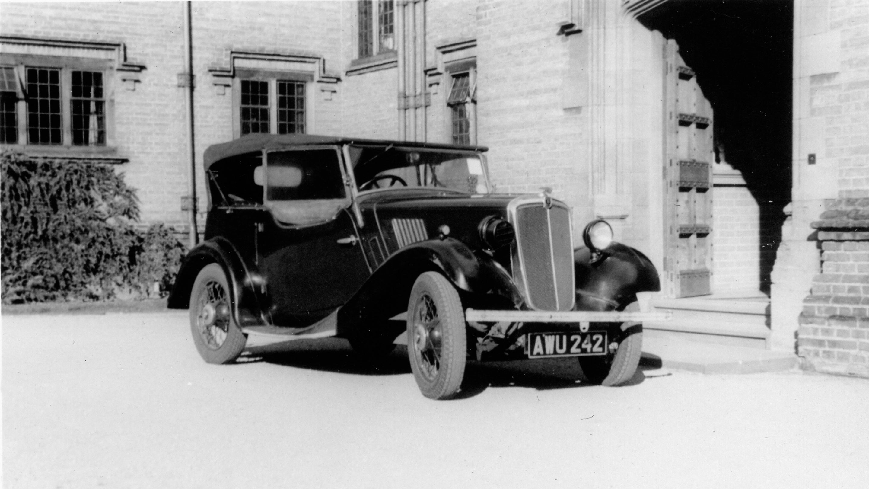 Black and white photo of an old fashioned car near a large open door