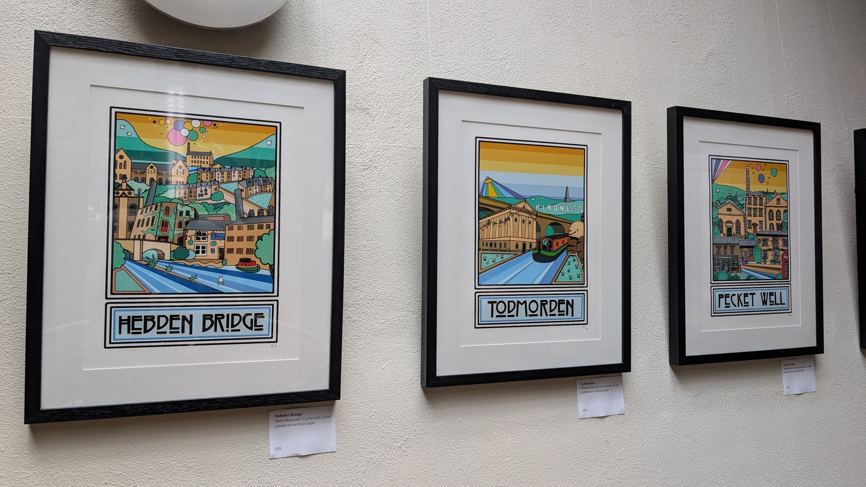 Colourful prints of local heritage buildings hang in a line on a white wall