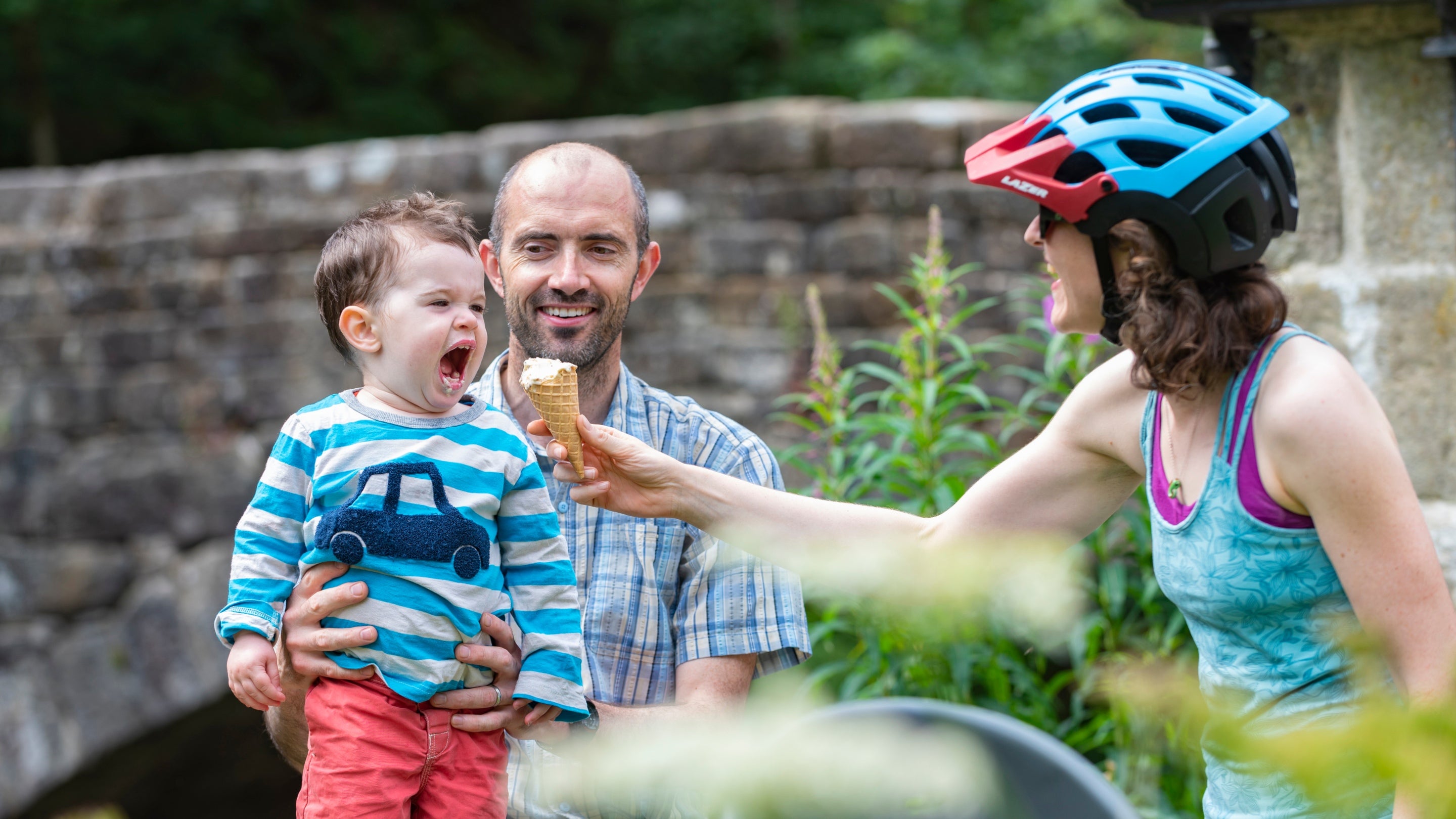 A woman feeding a young child an ice cream at Hardcastle Crags while a man looks on